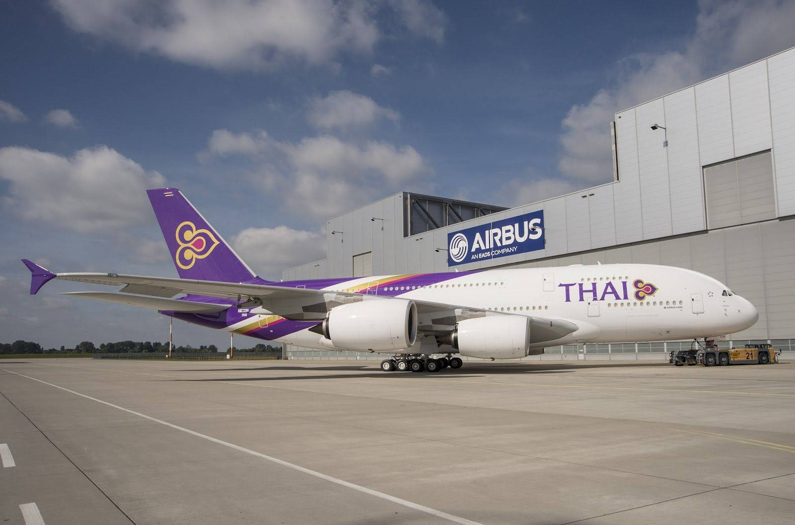 泰國航空空中巴士A380停泊在機場機庫旁，天空湛藍。