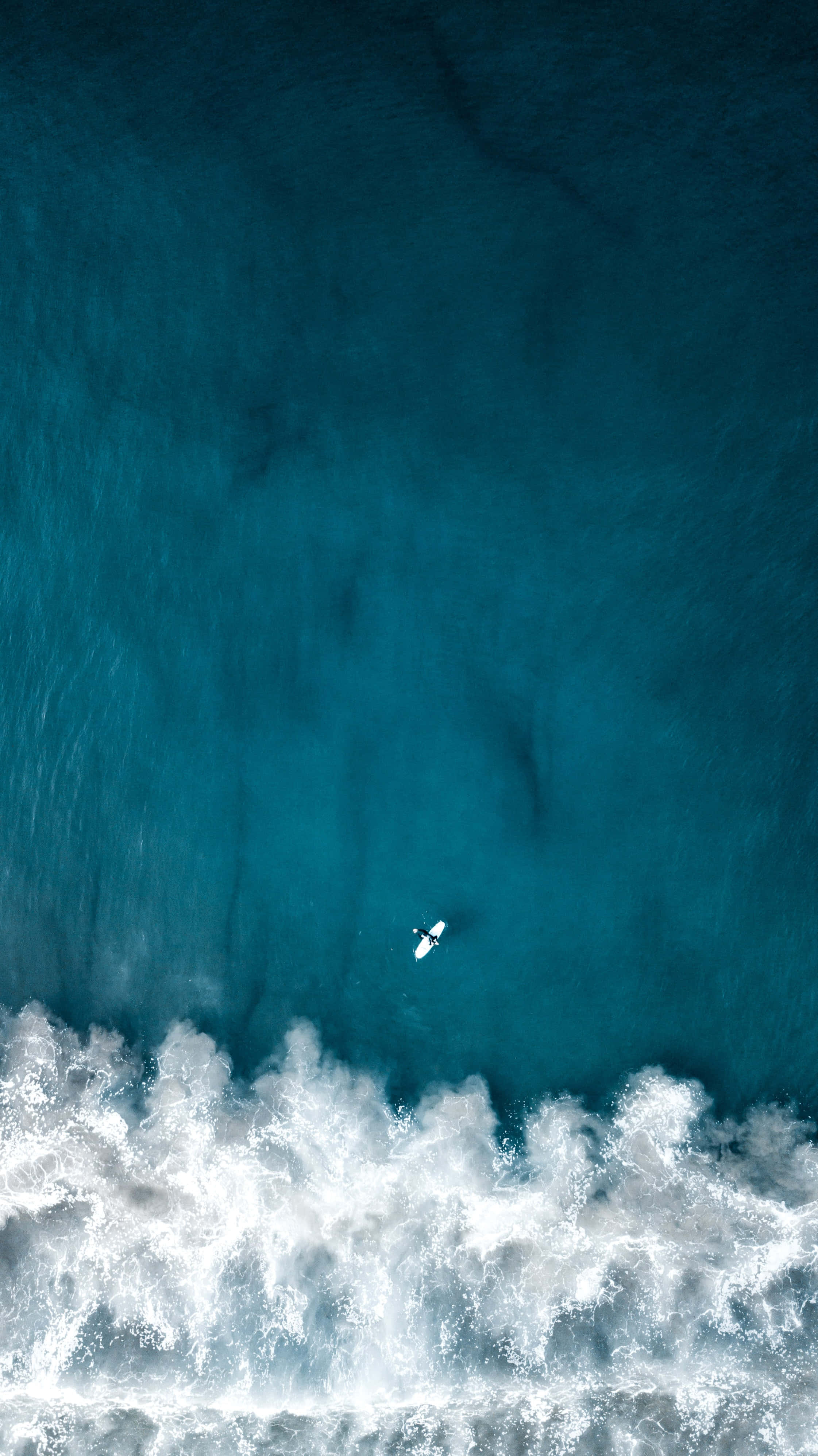 空中航拍海洋 iPhone 背景 壁紙 — 一位孤獨的衝浪者在碧綠色的海浪上滑行，白色泡沫從空中視角在下方破碎。