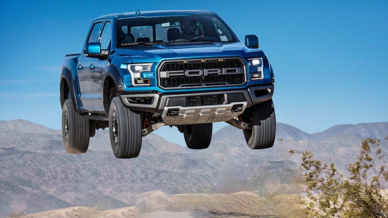空中飛躍的福特Raptor 壁紙 — 一輛充滿活力的藍色福特 F-150 Raptor 卡車在沙漠景觀上空飛躍，背景有山脈。