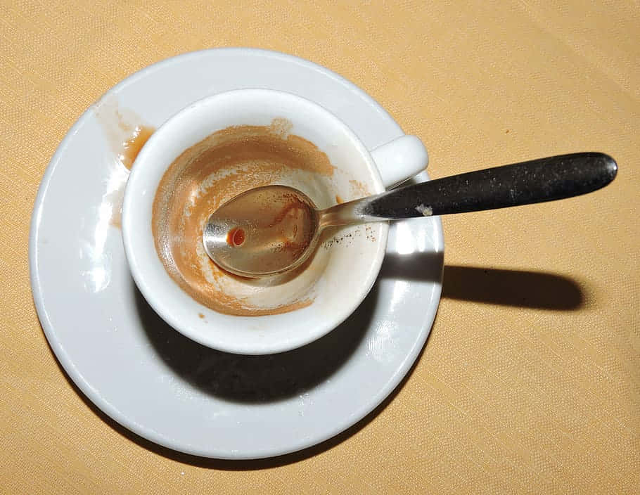 空咖啡杯與茶匙 壁紙 — 一個空的白色濃縮咖啡杯配湯匙，放在有紋理的米色桌布上的碟子上。