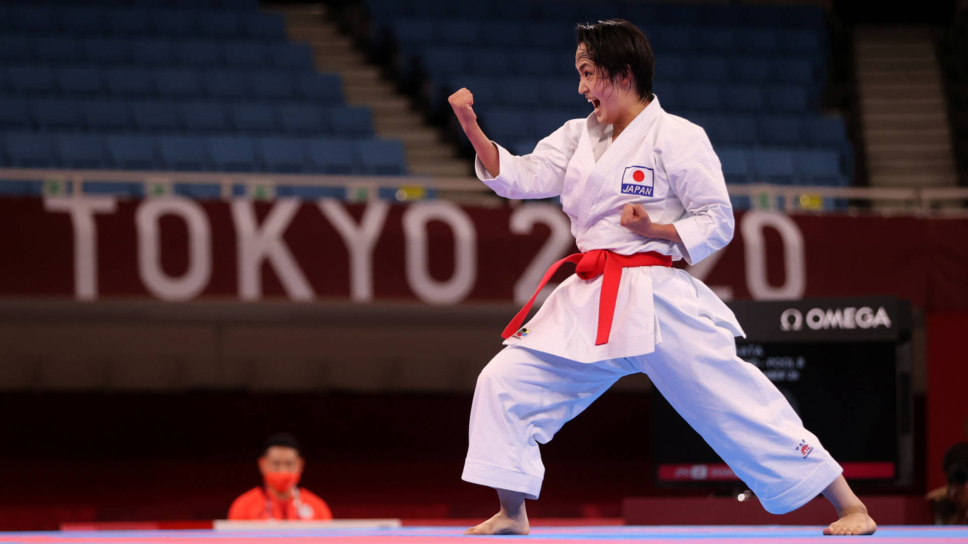 空手道選手清水基雄的型表演 壁紙 — 一位身穿白色道服、繫紅色腰帶的女空手道運動員在東京2020比賽期間於藍色軟墊上強力出擊。