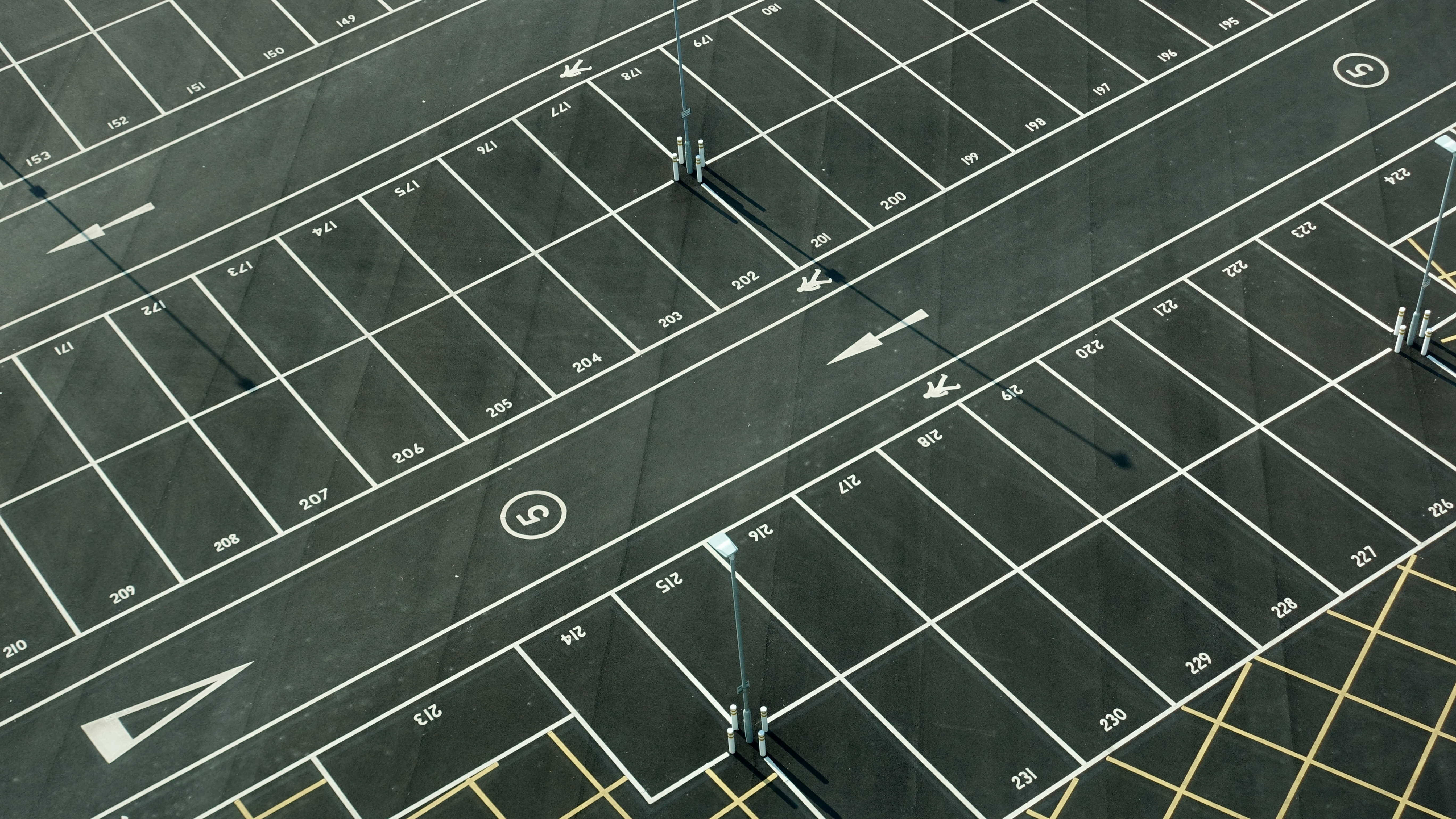 空曠乾淨的停車場 壁紙 — 空蕩蕩的瀝青停車場鳥瞰圖，帶有白色編號線和方向箭頭，在明亮的日光下。
