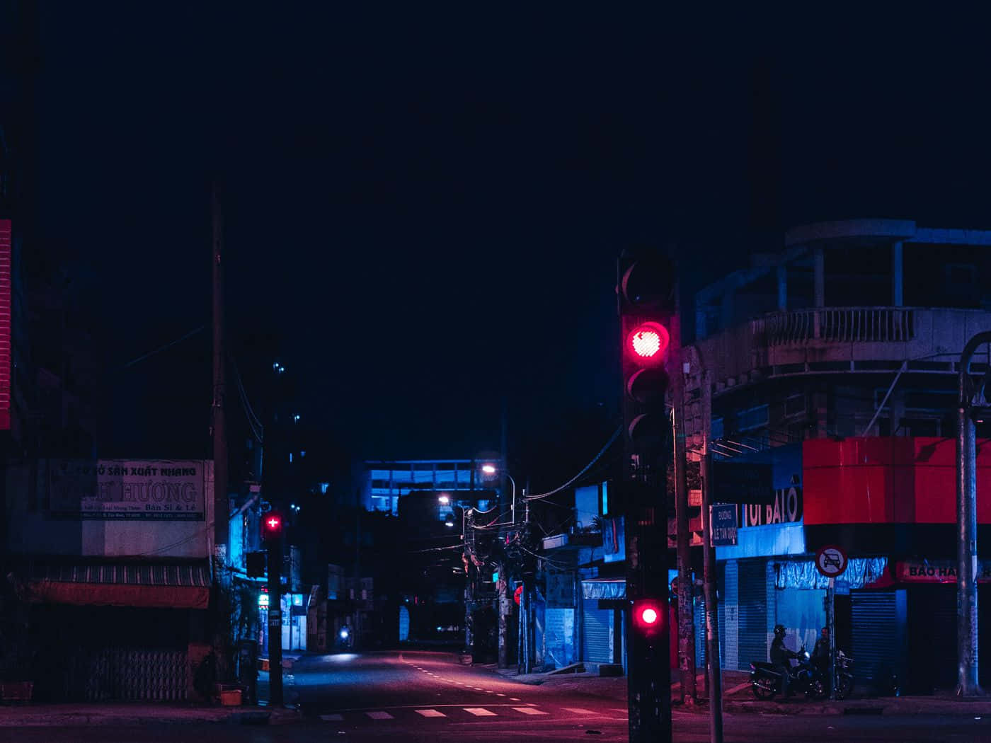 夜晚一條霓虹燈照亮的城市街道，有紅色交通燈和關閉的商店。