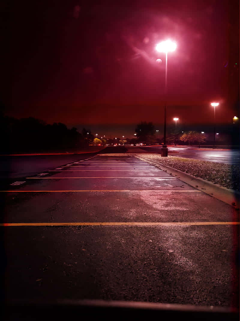 紅色燈光下的夜晚空停車場，濕滑路面和遠處樹木。