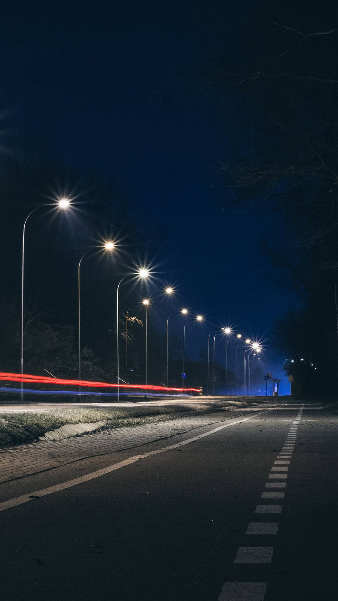 夜晚街道，有發光的燈和來往車輛留下的紅色光跡。
