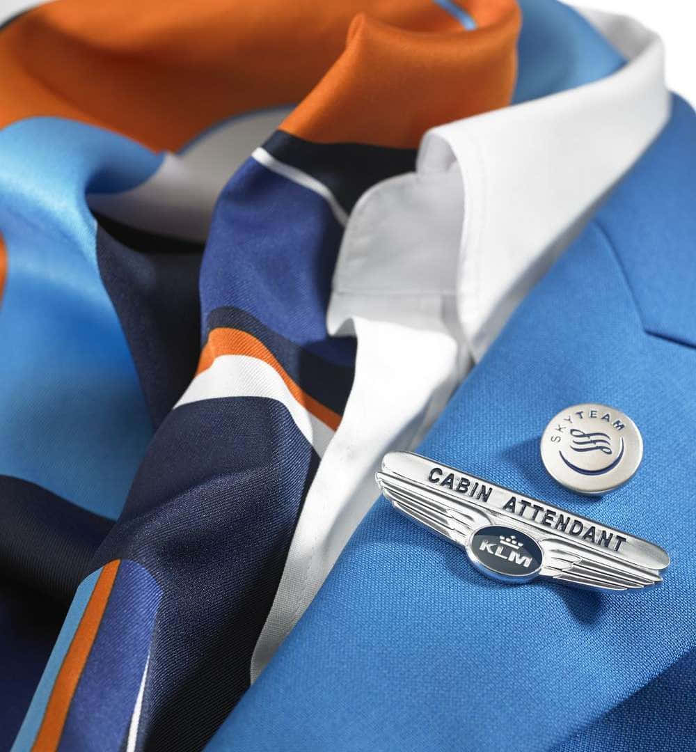 空服員的優雅制服照 壁紙 — KLM 機艙服務員藍色制服外套近照，配有 SkyTeam 襟章及橙藍間條絲巾。