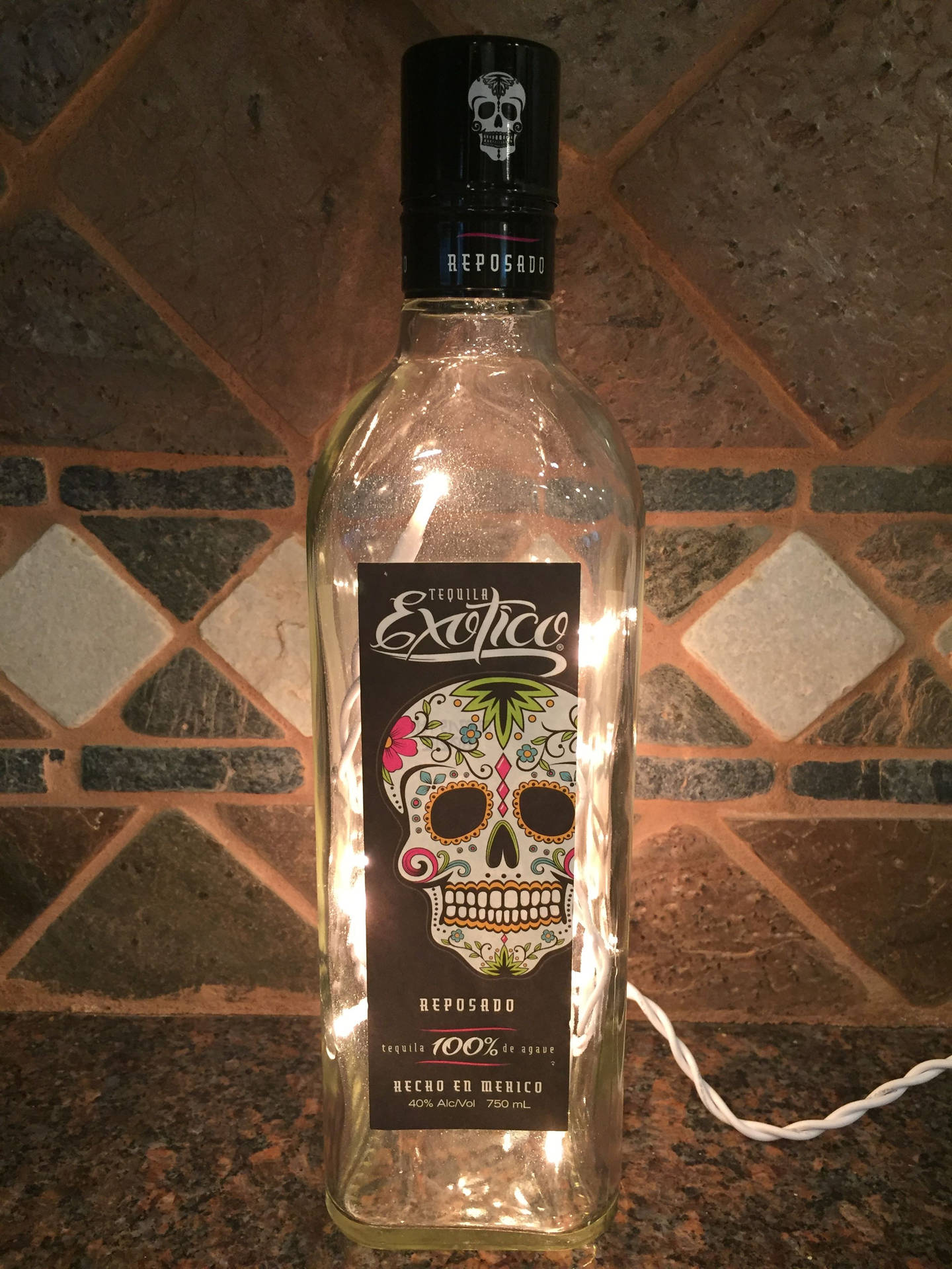 一個裝飾的龍舌蘭酒瓶，由串燈照亮，背景是瓷磚牆。