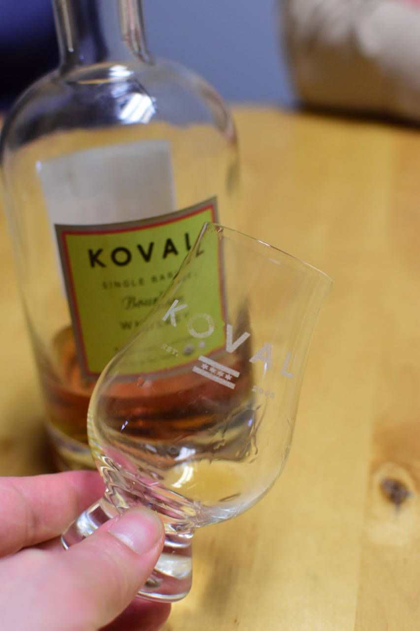 手揸住Koval威士忌品酒杯，背景有酒樽。