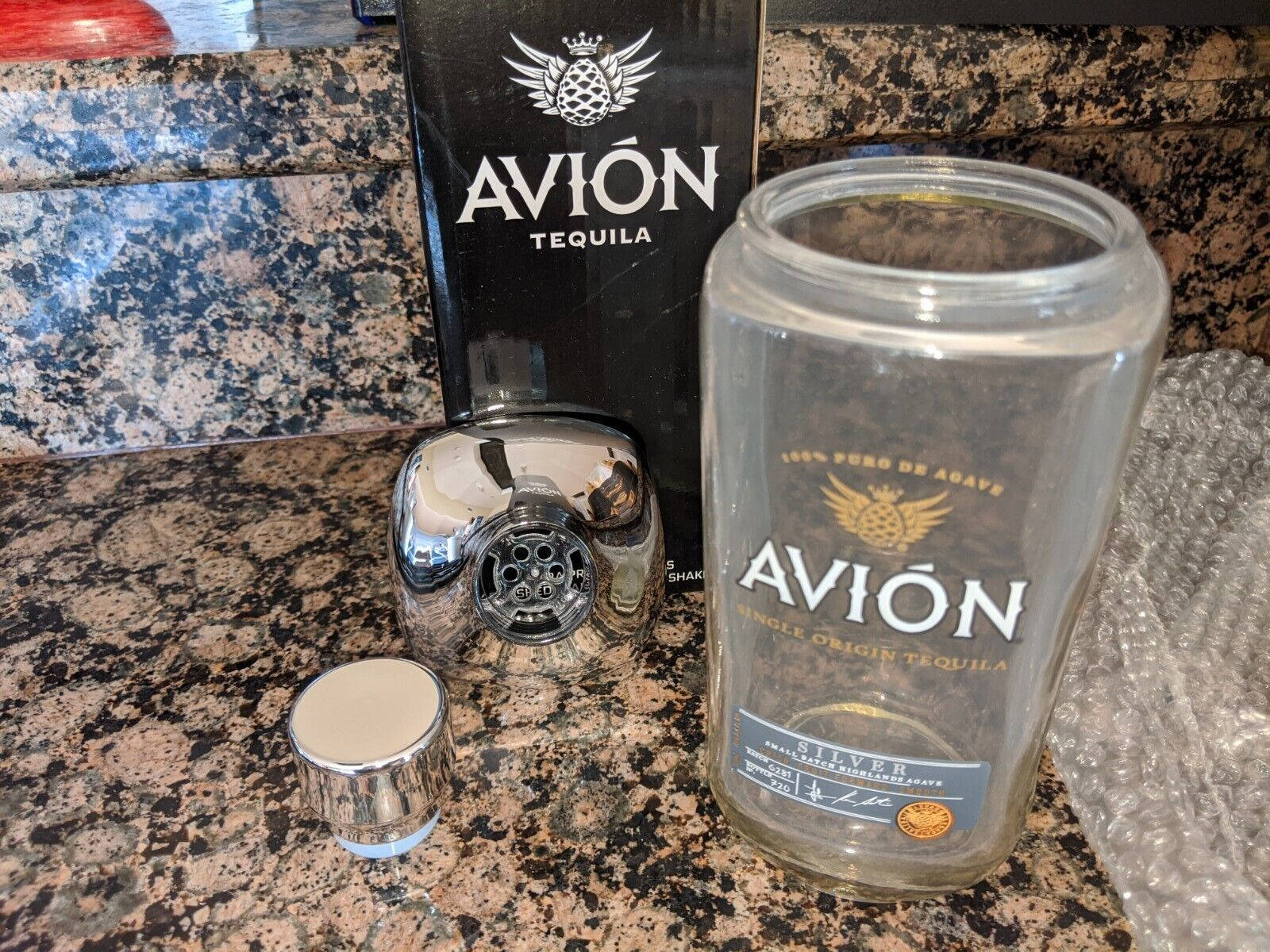 鍍鉻雞尾酒調酒器和空龍舌蘭酒瓶在花崗岩檯面上。