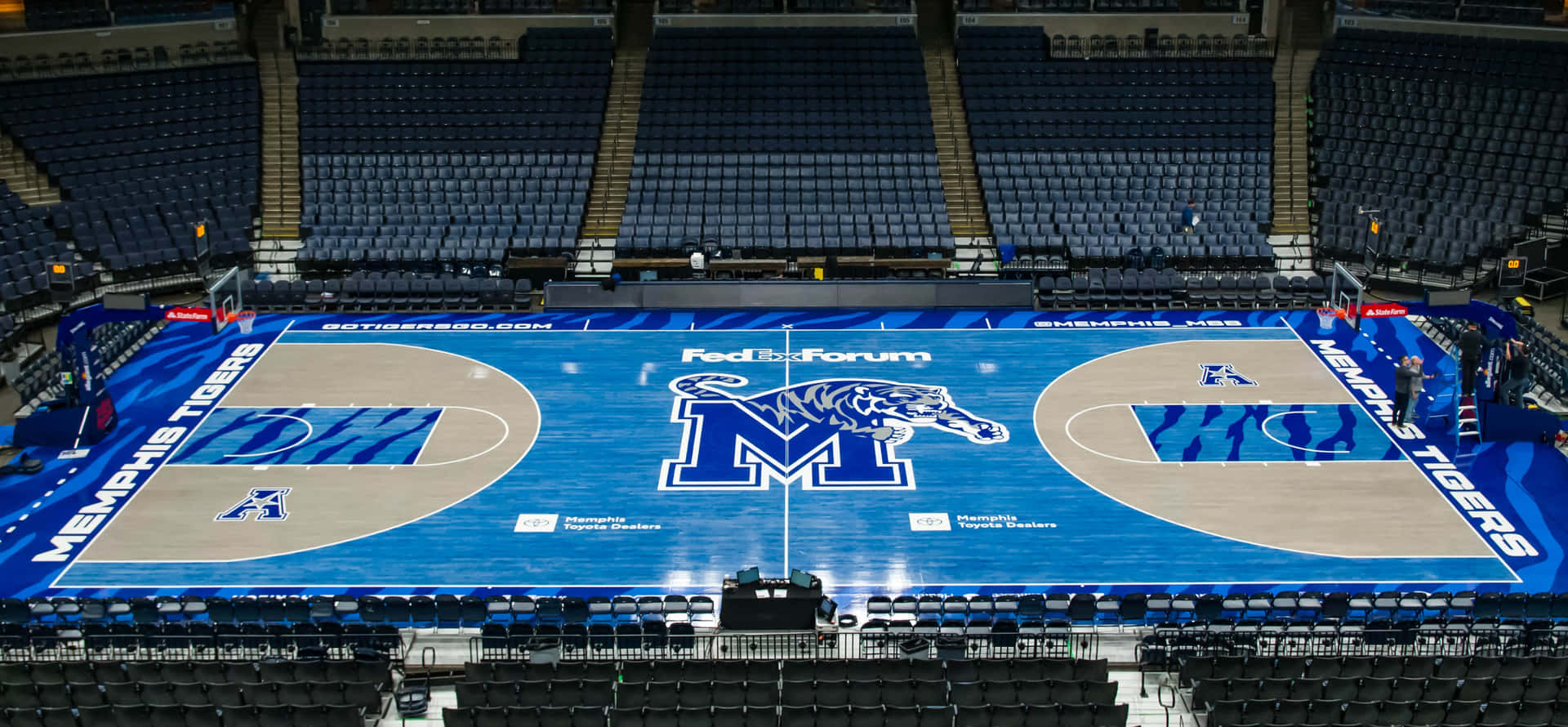 空籃球場圖片 壁紙 — FedExForum 內空無一人的孟菲斯老虎隊籃球場的鳥瞰圖，採用藍色和米色設計，周圍是深色座位。