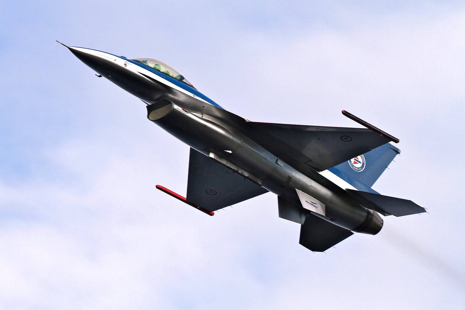 空軍 F-16 壁紙 — 一架流線型戰鬥機在淡藍色天空和縷縷白雲中向上翱翔。