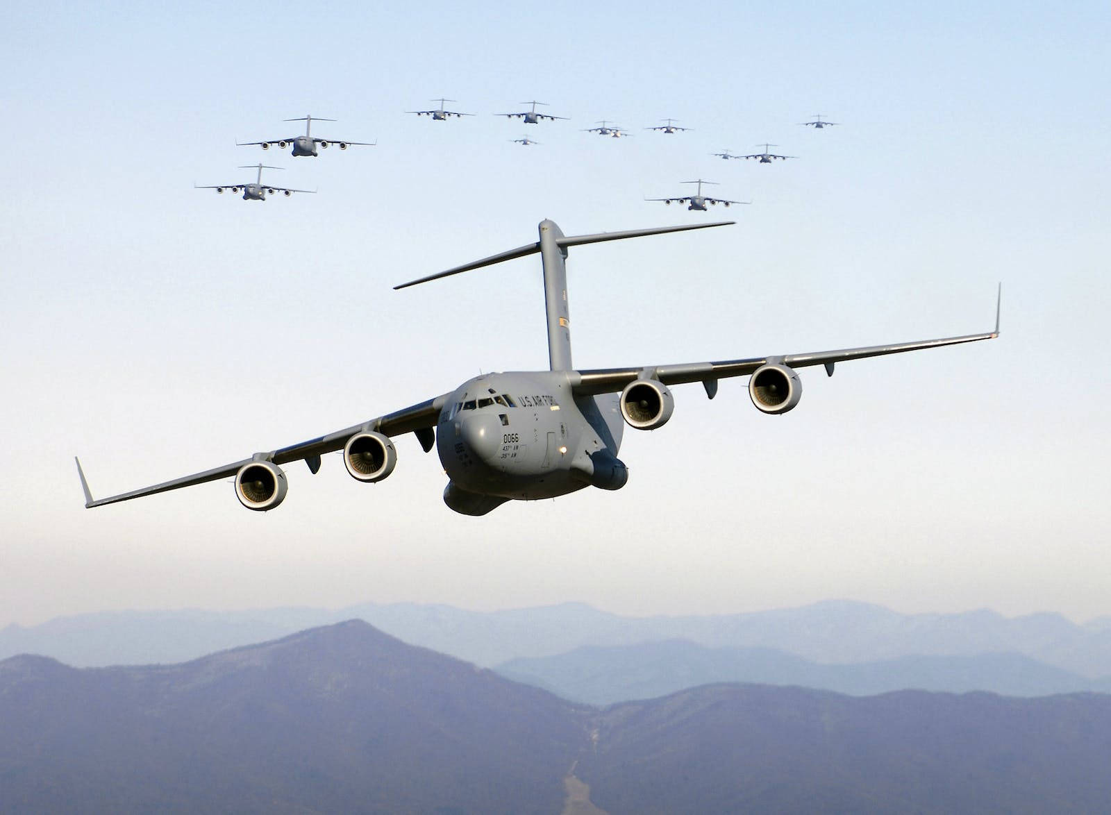 空軍 Globemaster 轟炸機 壁紙 — 一隊灰色軍用運輸機在淡藍色天空下，以精確編隊飛越山脈。