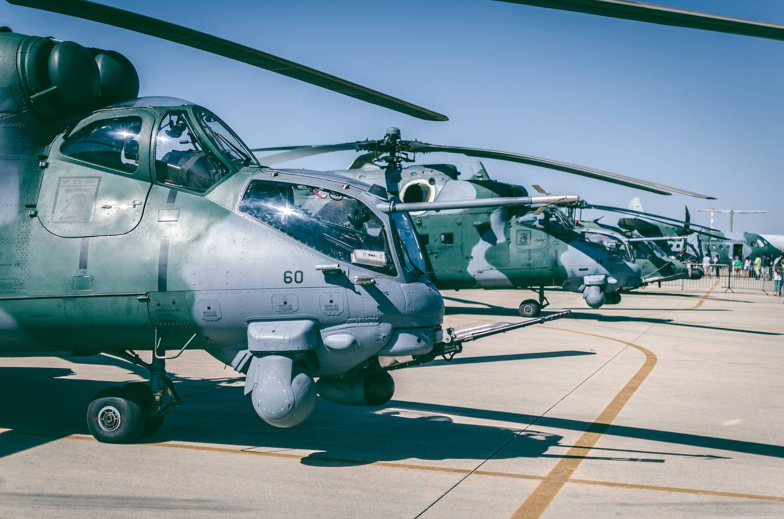 空軍直升機 壁紙 — 一排軍用直升機停泊在陽光明媚的停機坪上，天空清澈湛藍，陰影清晰。