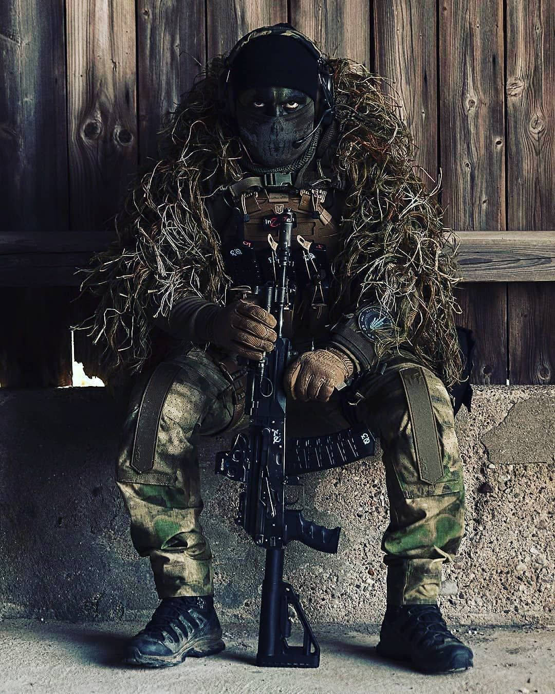 一名迷彩士兵手持步槍靠在木牆上。