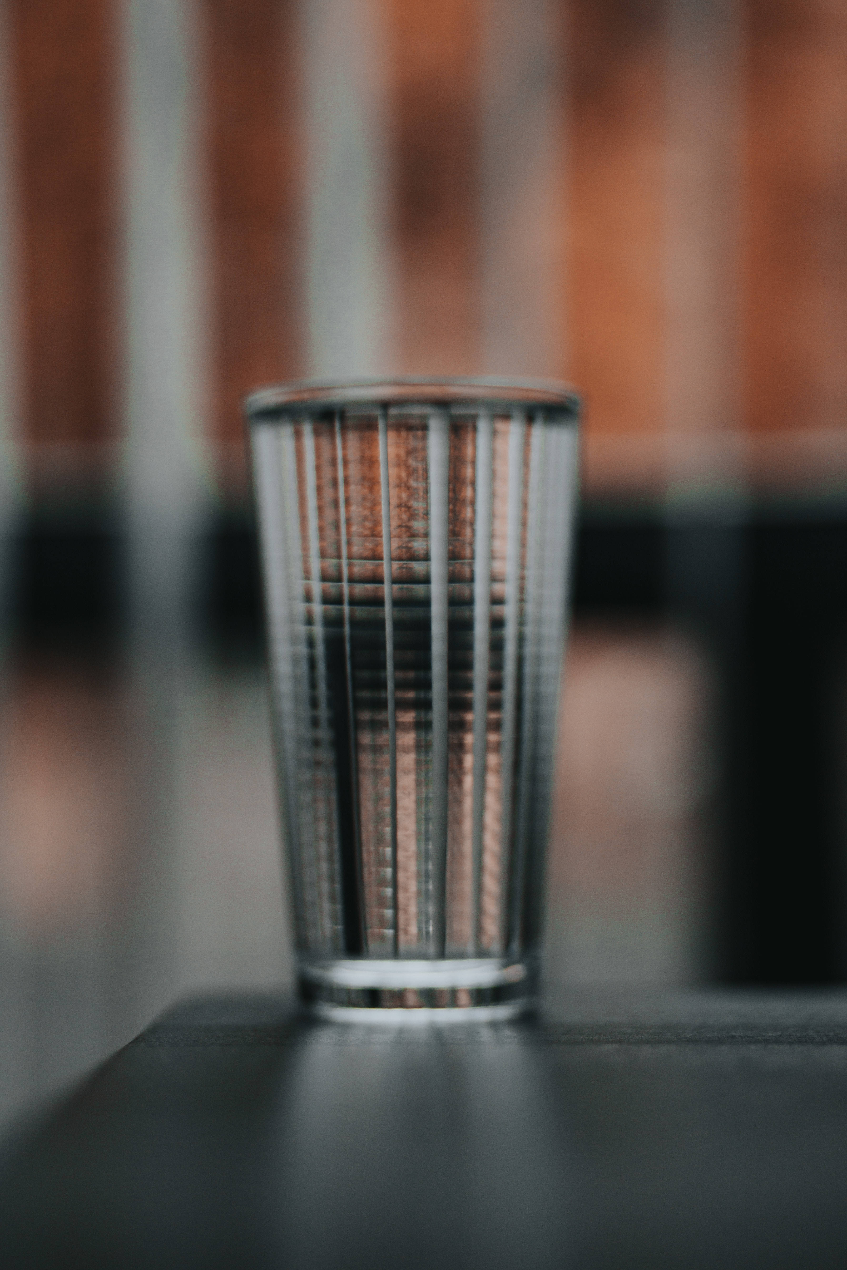 空高腳杯選擇性焦點 壁紙 — 一個透明帶棱紋的飲水杯放在深色表面上，背景是模糊的磚牆。