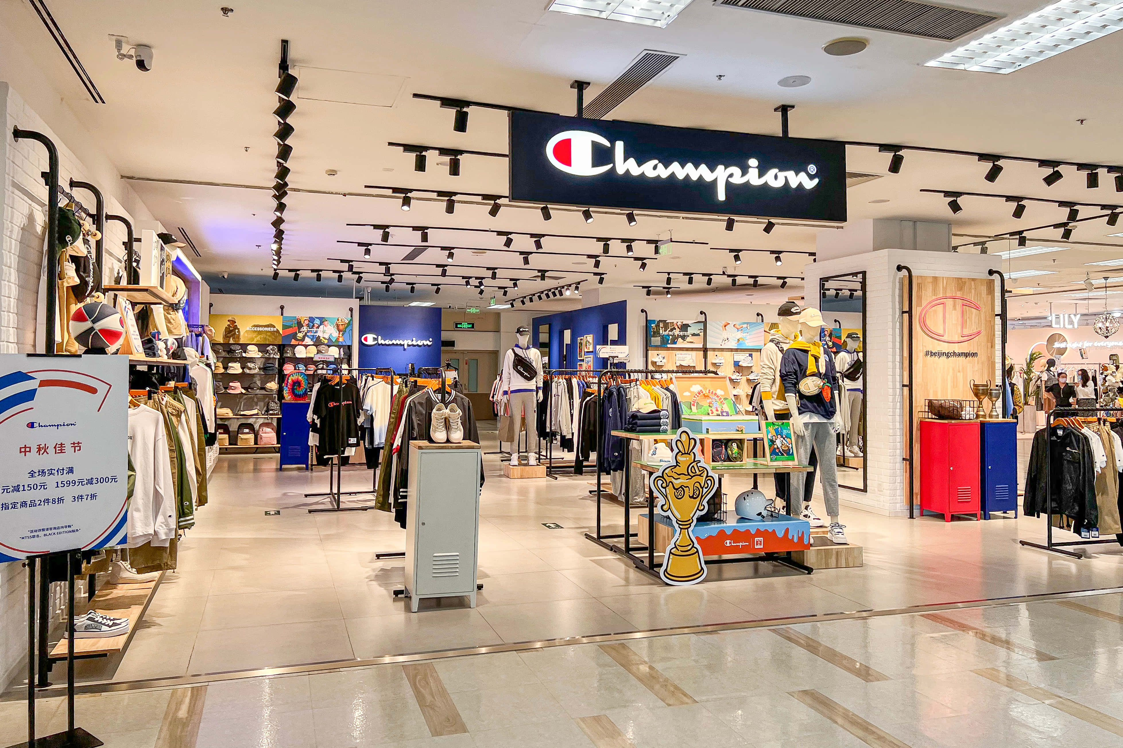 穿上 Champion，感受無敵自信 壁紙 — 光線明亮的Champion運動服飾店，展示人體模型、貨架和促銷展示，配以現代天花板燈光。