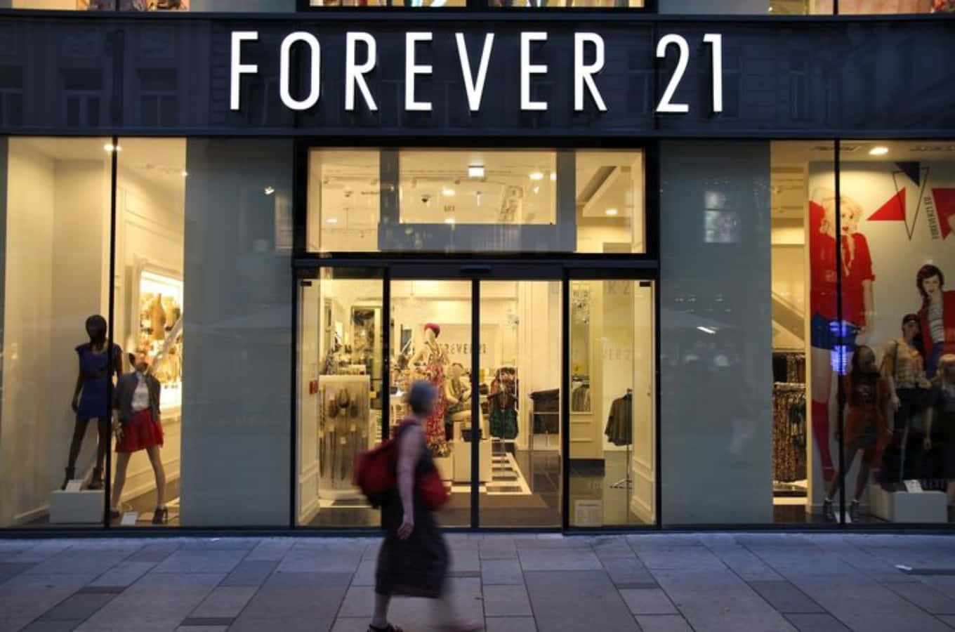 穿上 Forever 21 最新到貨，展現時尚潮流風範 壁紙 — 黃昏時分，一個人走過燈光明亮的Forever 21商店，櫥窗裏的模特兒展示色彩繽紛的服裝。