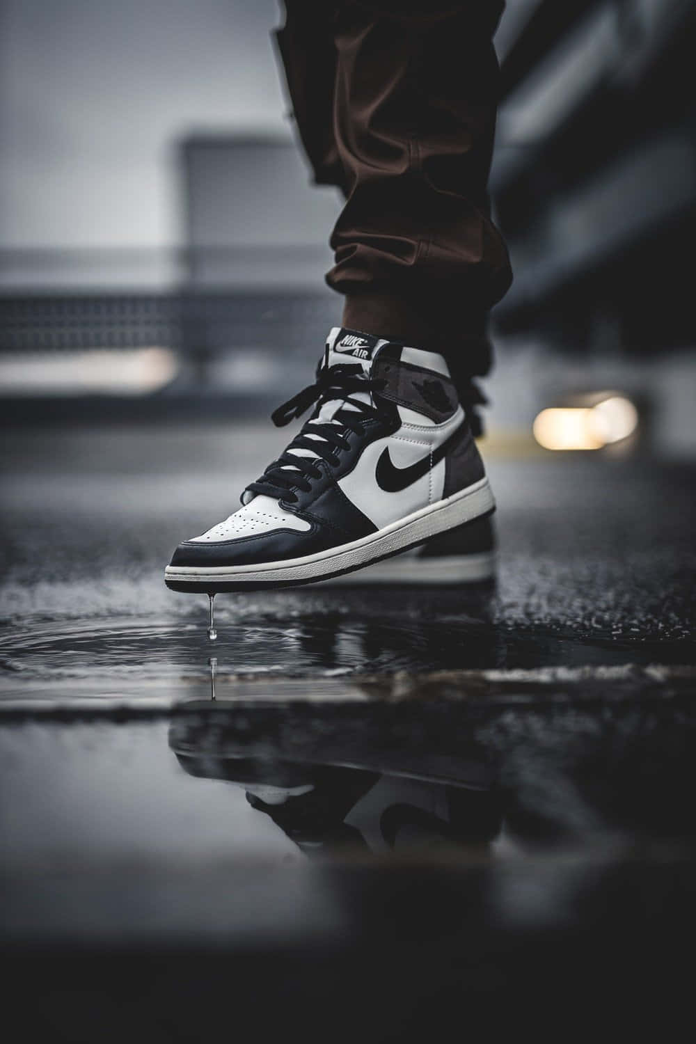 穿上Air Jordan，展現你的時尚風格 壁紙 — 一對黑白Nike運動鞋的特寫，水滴落在濕漉漉的城市路面上，背景是模糊的城市燈光。
