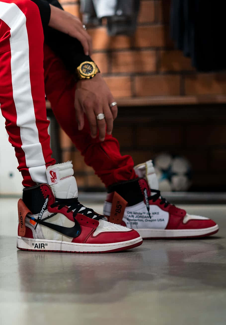穿上Air Jordan，提升你的表現 壁紙 — 一個人穿著紅白色 Off-White x Nike Air Jordan 1 運動鞋，戴著金錶和戒指的特寫。
