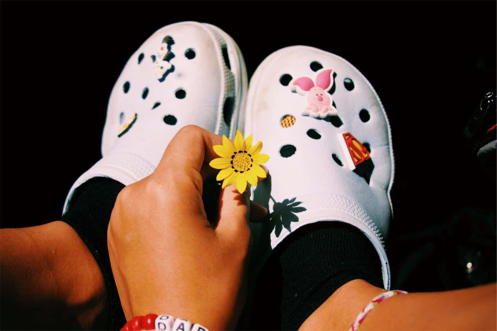 手在裝飾過的白色Crocs附近拿著一朵黃花。