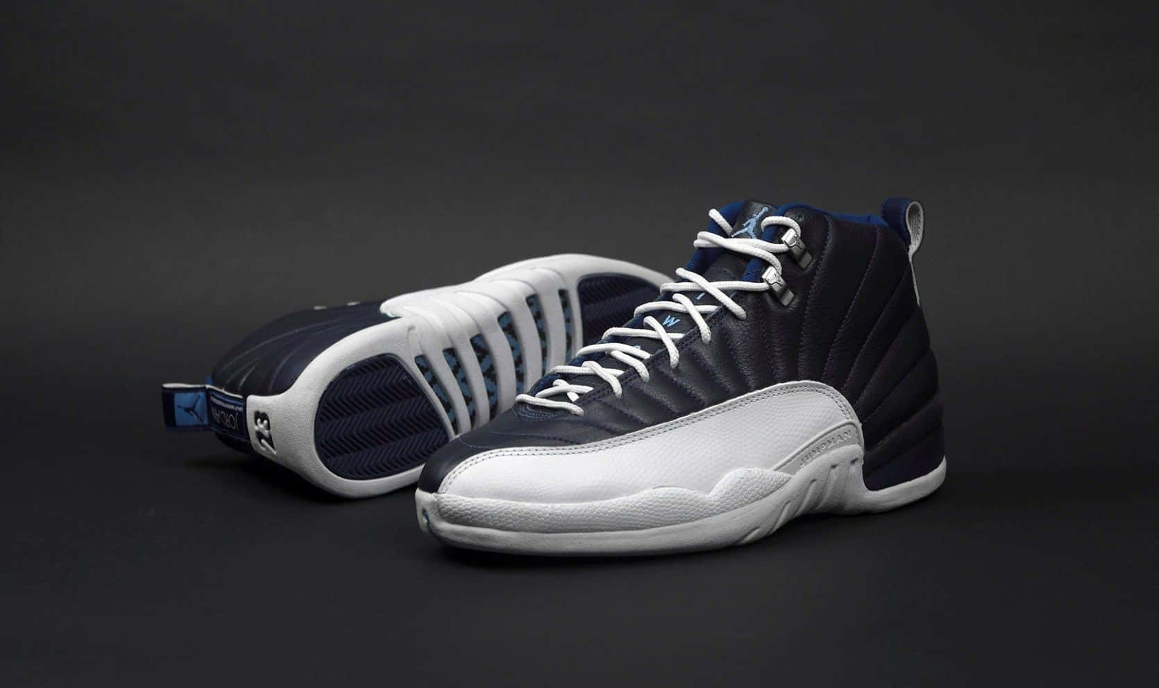 穿上經典 Nike Air Jordan，展現你的風格 壁紙 — 一對海軍藍和白色高筒運動鞋，配有白色鞋帶，在深灰色工作室背景上展示。