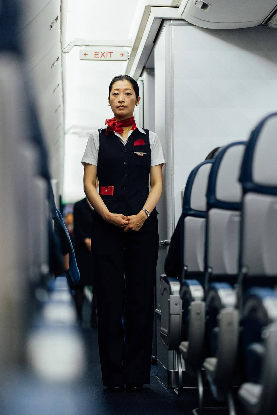 一位空中服務員站在飛機走廊中，座位排之間。