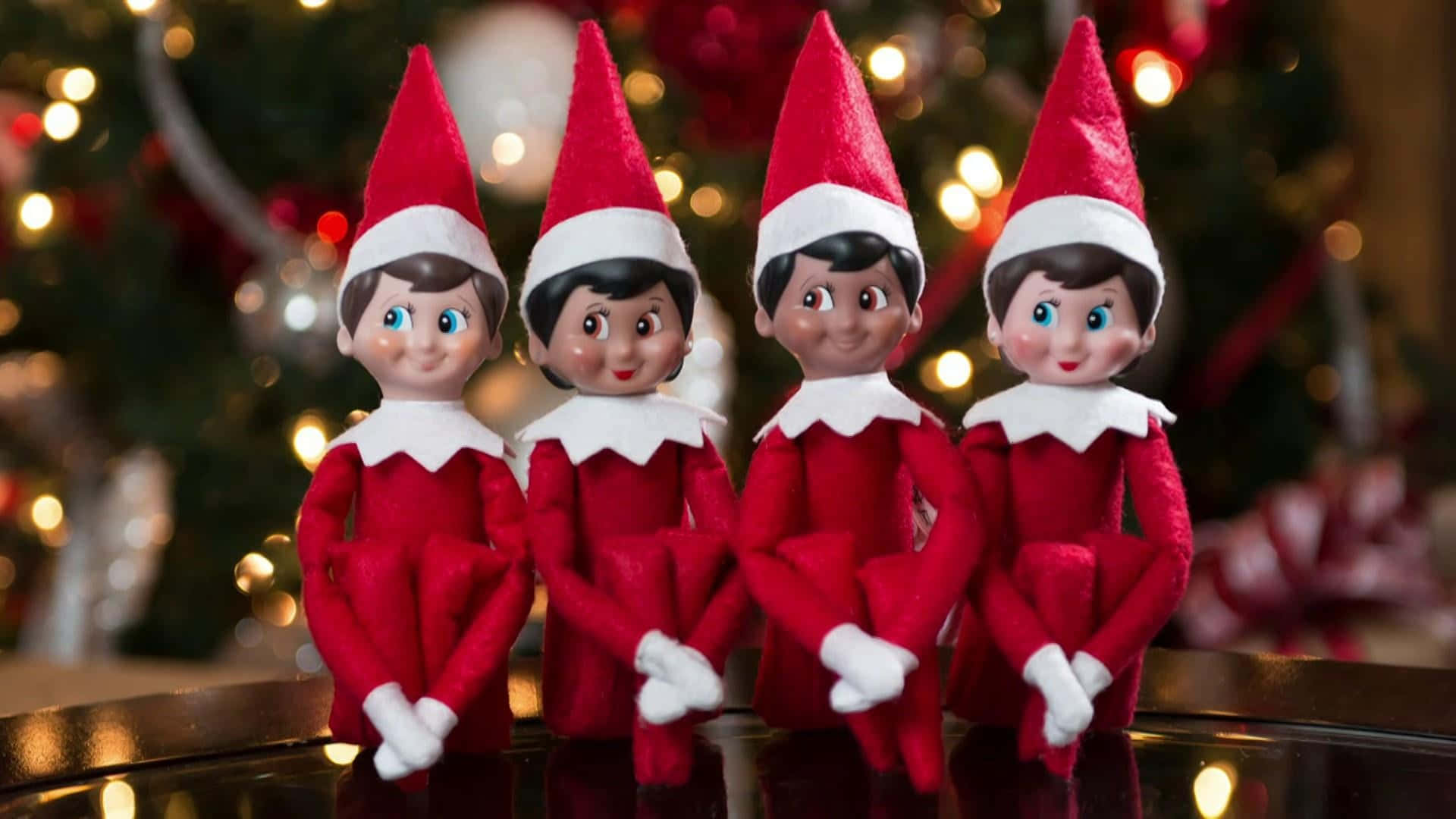 四個穿著紅白服裝的精靈公仔，一起坐在聖誕樹附近。