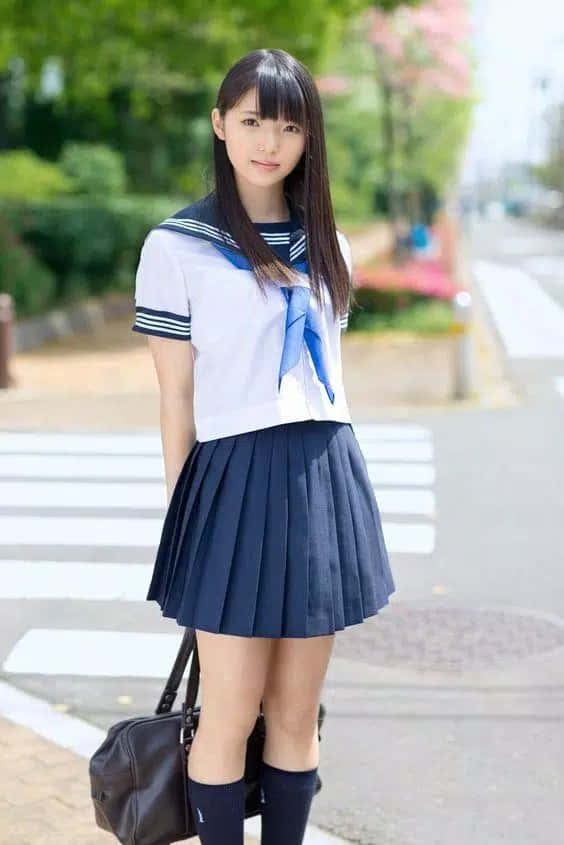 一位穿著水手服的日本女學生站在有櫻花的街道上。