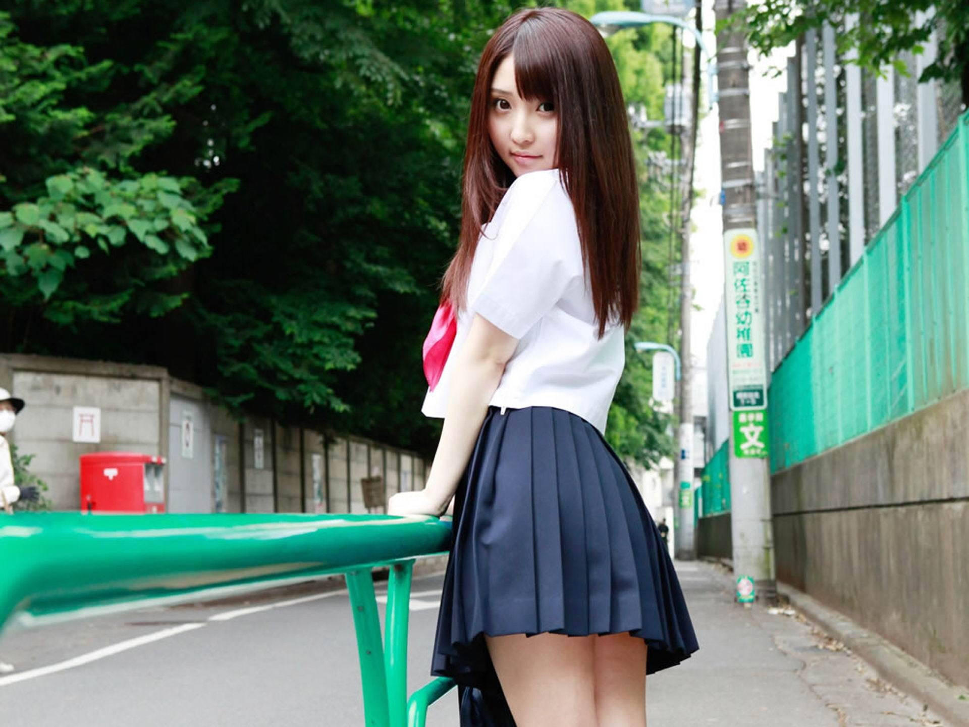 一位身穿校服的年輕女子在陽光明媚的街道上靠著綠色欄杆。