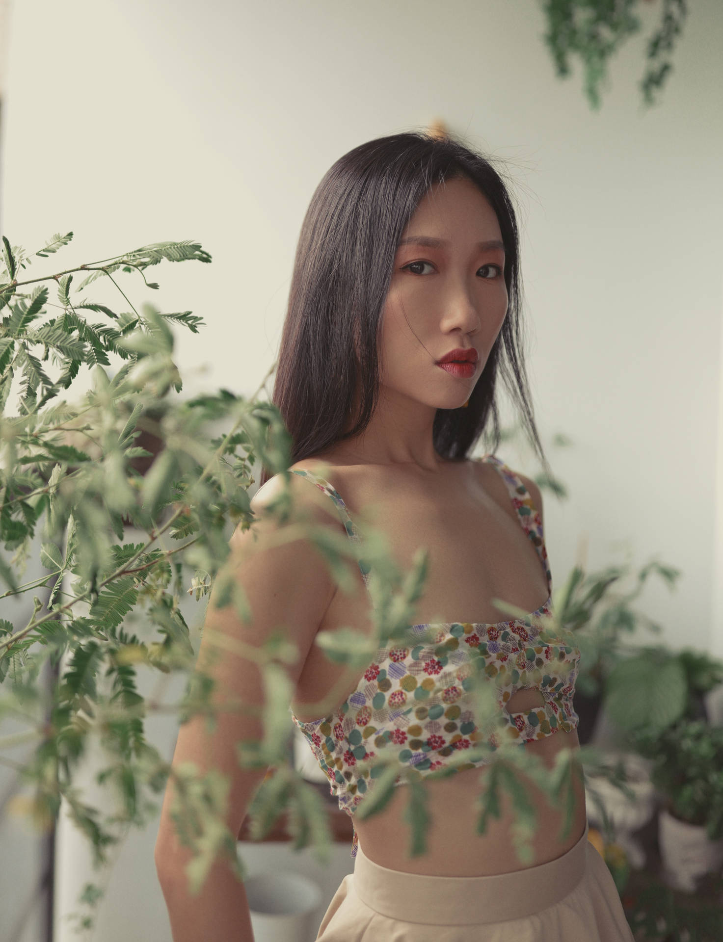 穿比基尼的纖瘦女孩 壁紙 — 一位身穿花卉短版上衣的女性站在茂密的綠色植物中，柔和自然光線穿透其間。