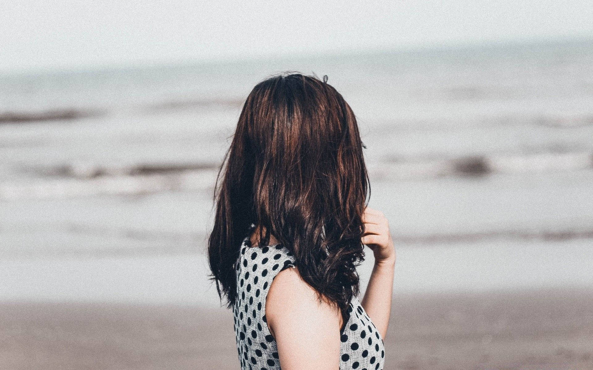 身穿波點裙的女子站在沙灘上面向海洋
