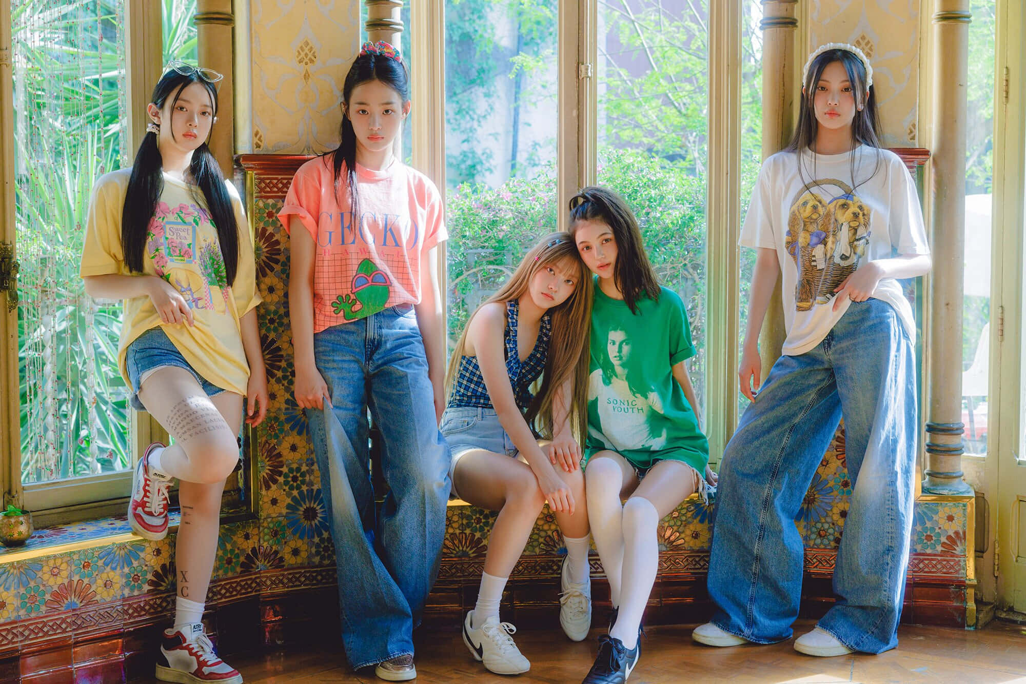 穿牛仔短褲與喇叭褲的女孩照片 壁紙 — 五位年輕女性穿著色彩繽紛的休閒服裝，在一個陽光充足、裝飾華麗、帶有大窗戶的房間裡，自信地坐在花卉圖案的長椅上擺姿勢。