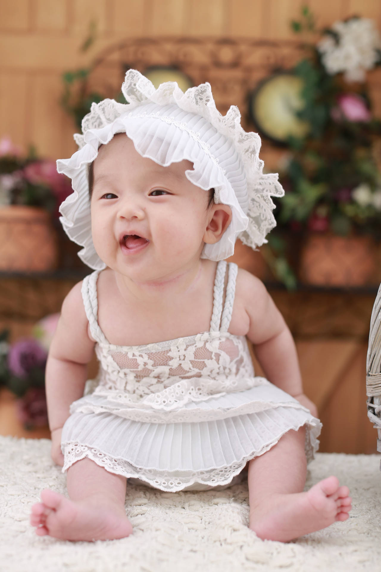 一個快樂的女嬰穿著白色蕾絲帽和裙子坐在地毯上。