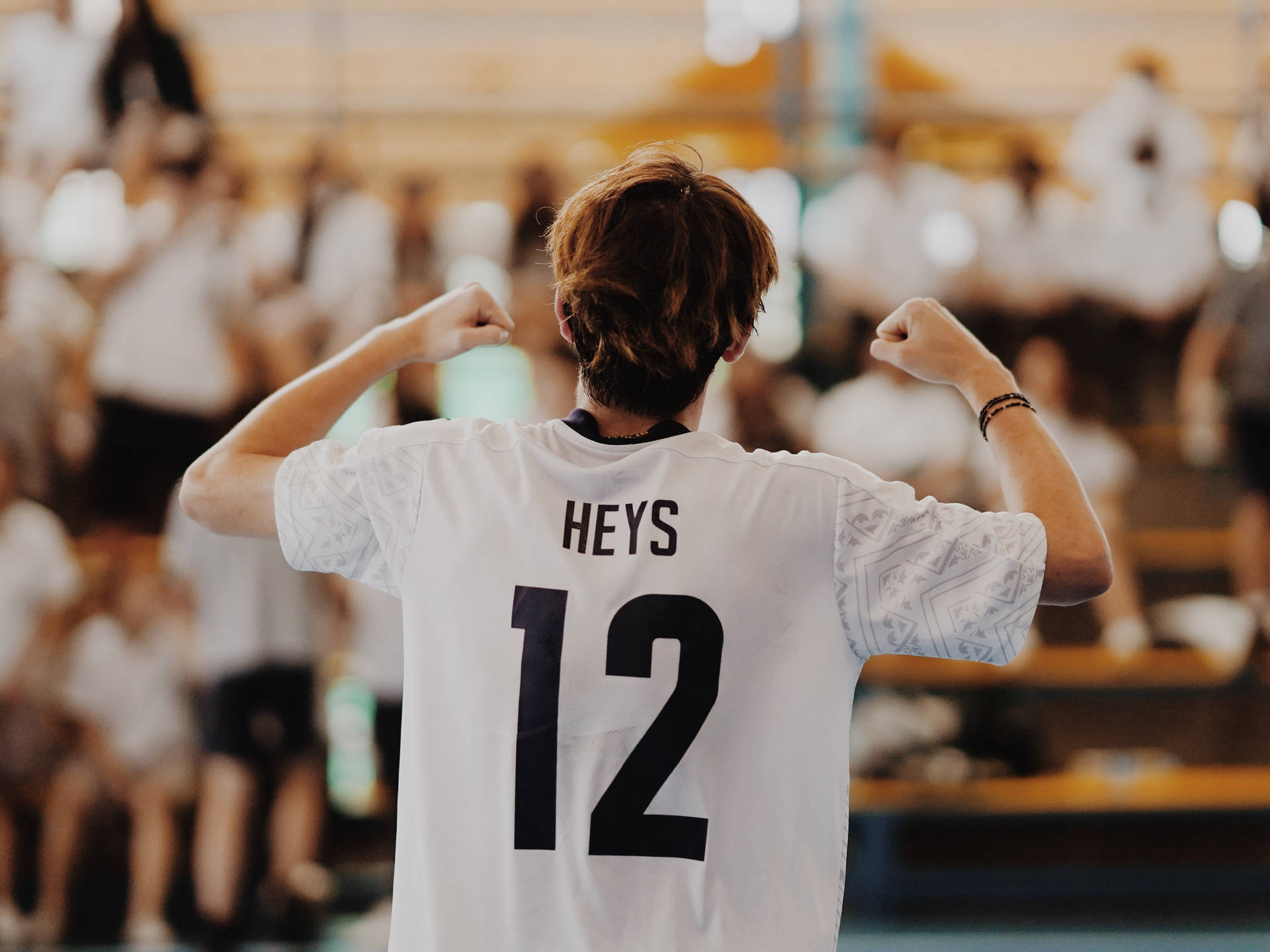 年輕運動員身穿白色球衣印有HEYS 12，在體育館內面對歡呼的人群彎曲手臂。