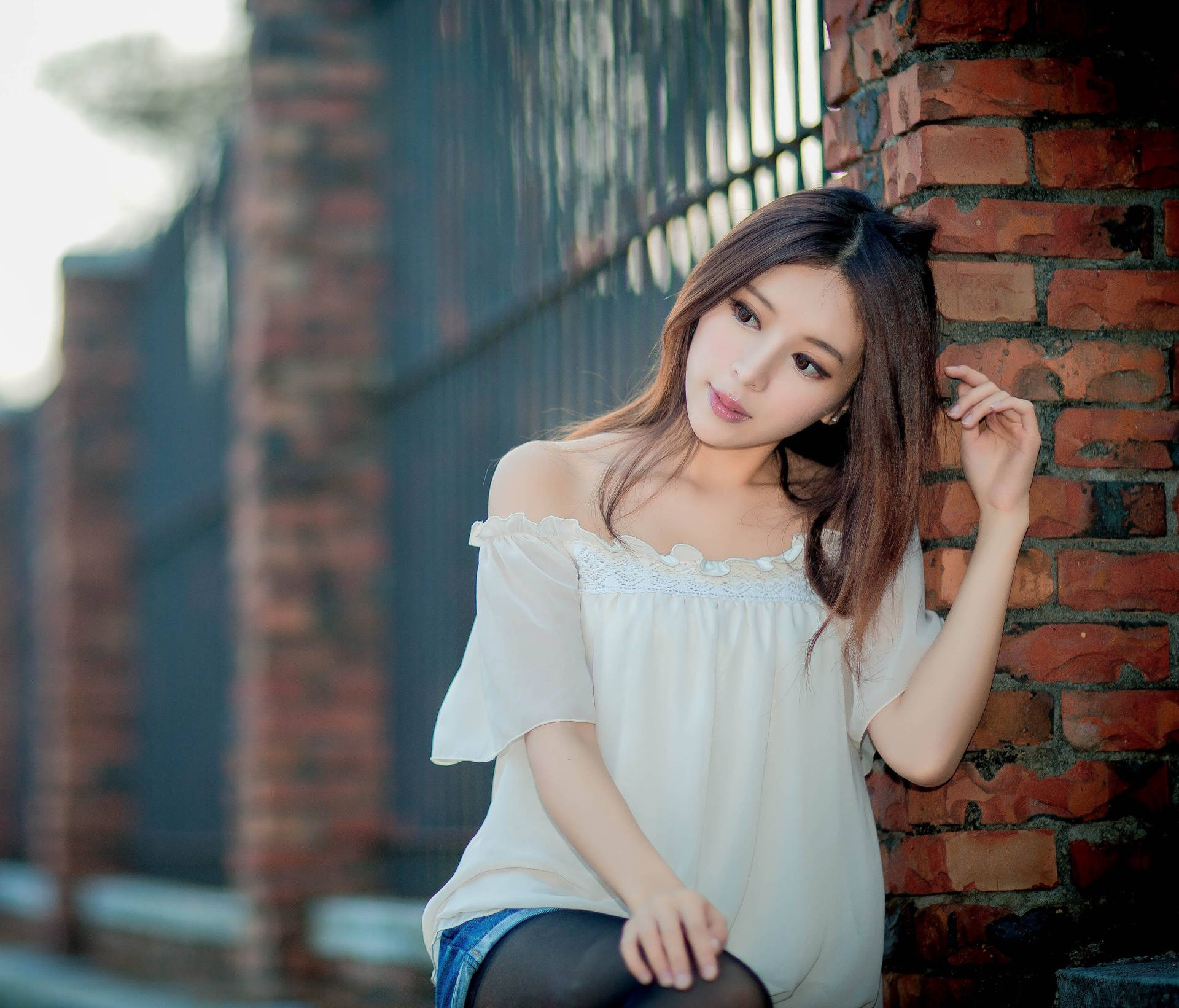 年輕女性身穿白色上衣靠喺戶外磚牆上