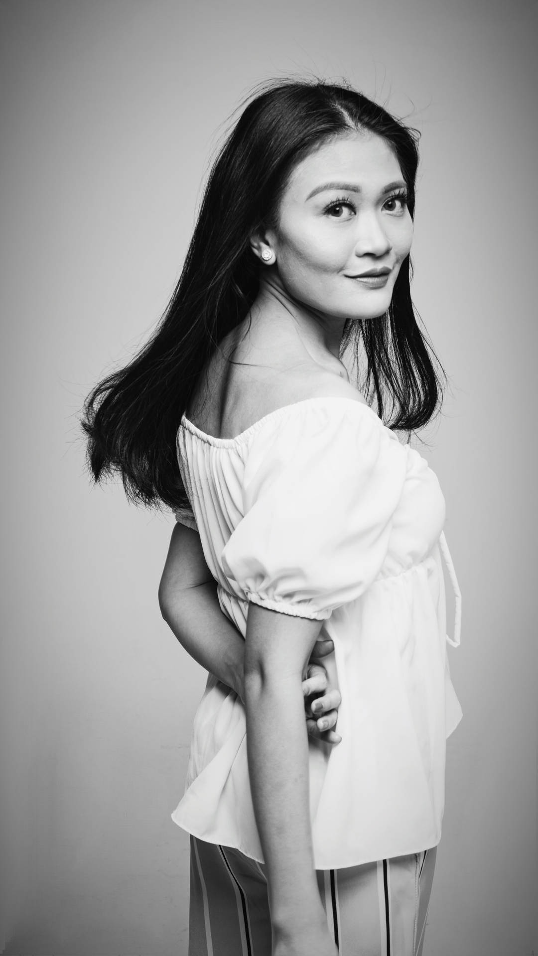 一位穿著白色露肩襯衫的女性在攝影棚中擺姿勢微笑。