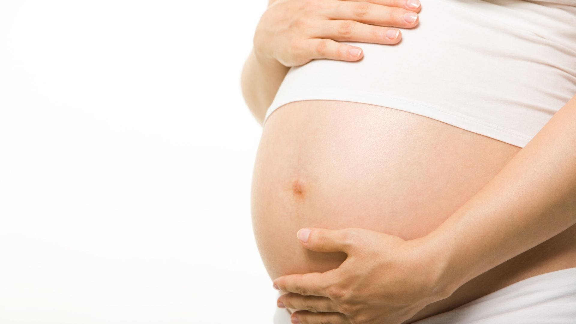 穿白衣孕婦特寫 壁紙 — 一位孕婦在潔白背景前用雙手輕輕捧著她圓潤的肚子。