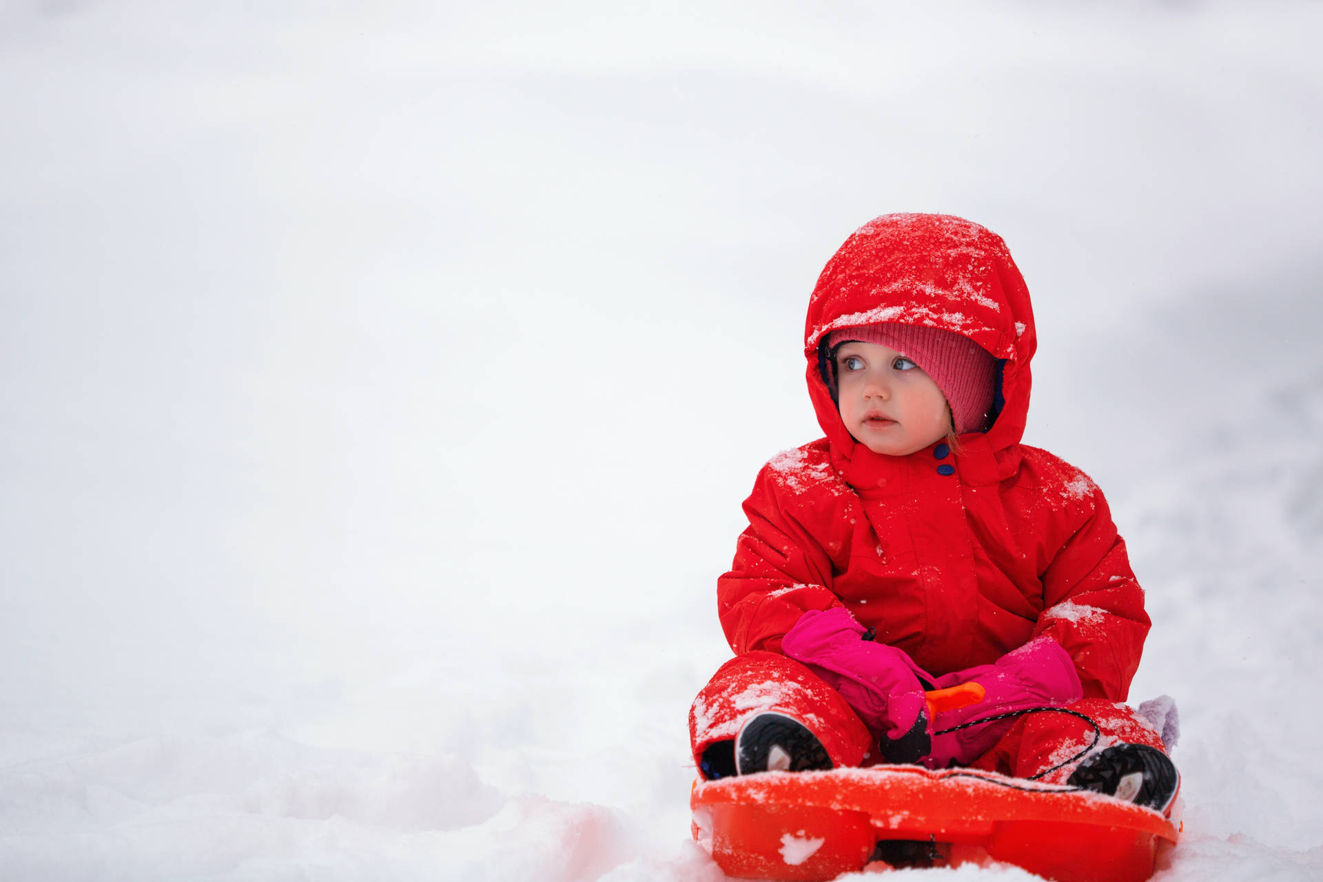 穿著紅色雪衣的小孩坐在雪地上的雪橇上