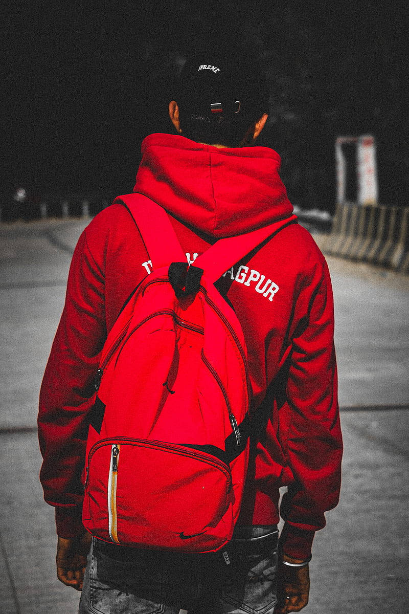 穿紅色夾克與背包的男孩 壁紙 — 一個穿著鮮紅色連帽衫和相配背包的人在夜間昏暗的城市街道上走開。