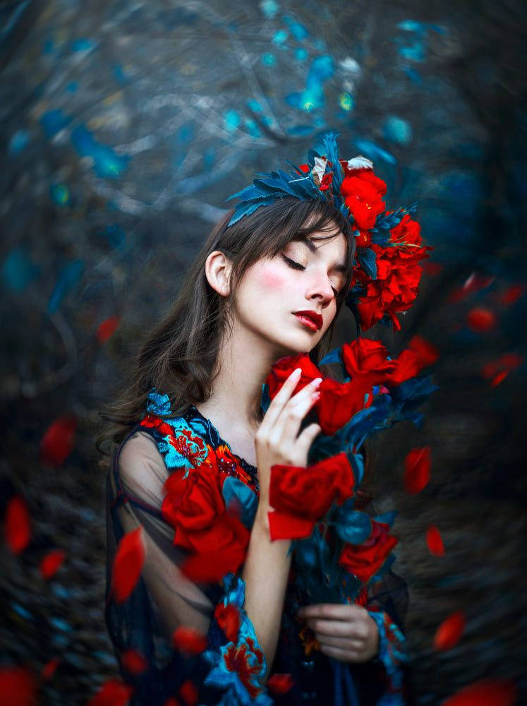 身穿紅藍色花卉服飾的女性，臉龐周圍有漂浮的花瓣。