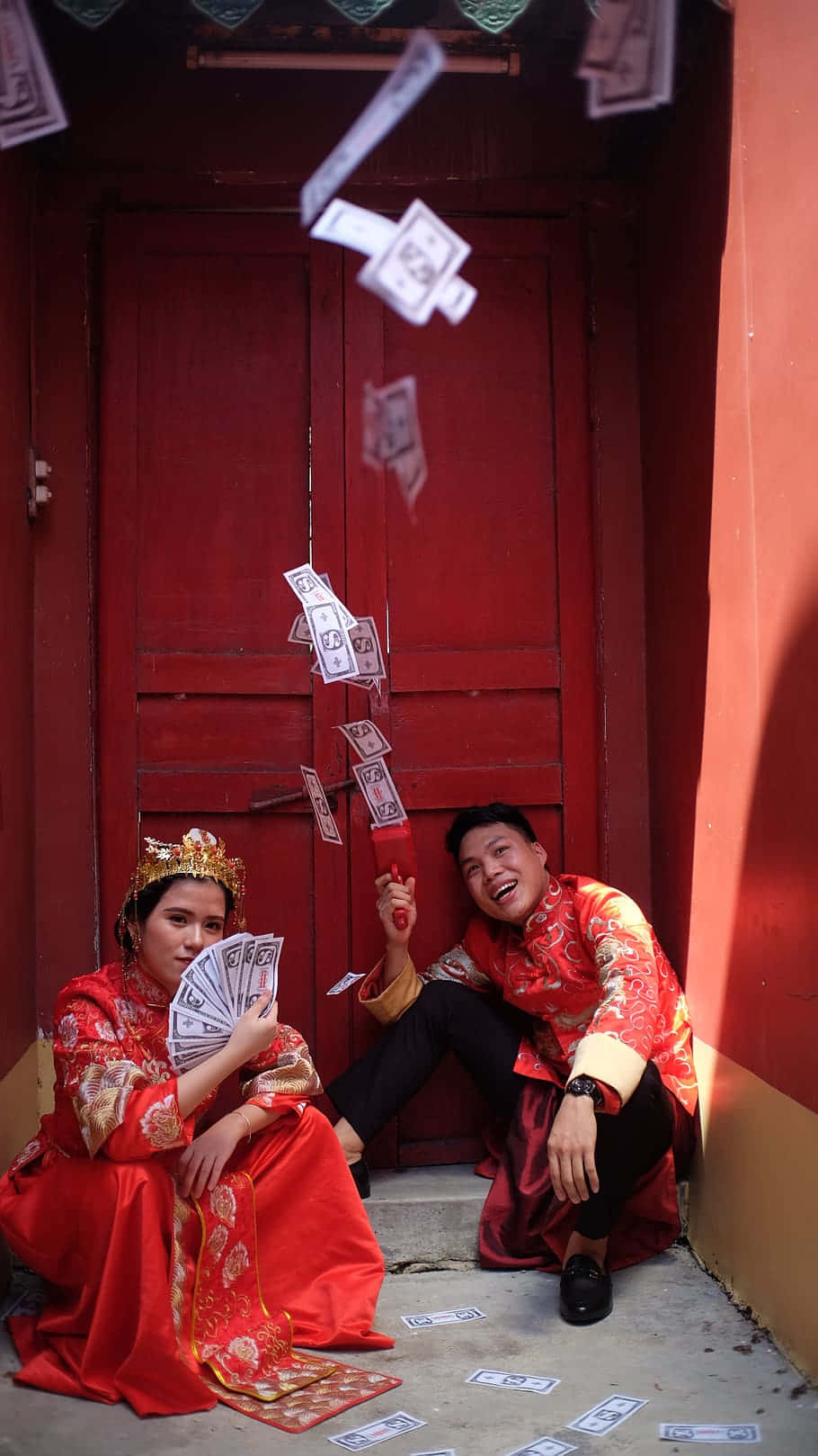 一對幸福的新人穿著紅色傳統服飾，被飄落的金錢包圍。