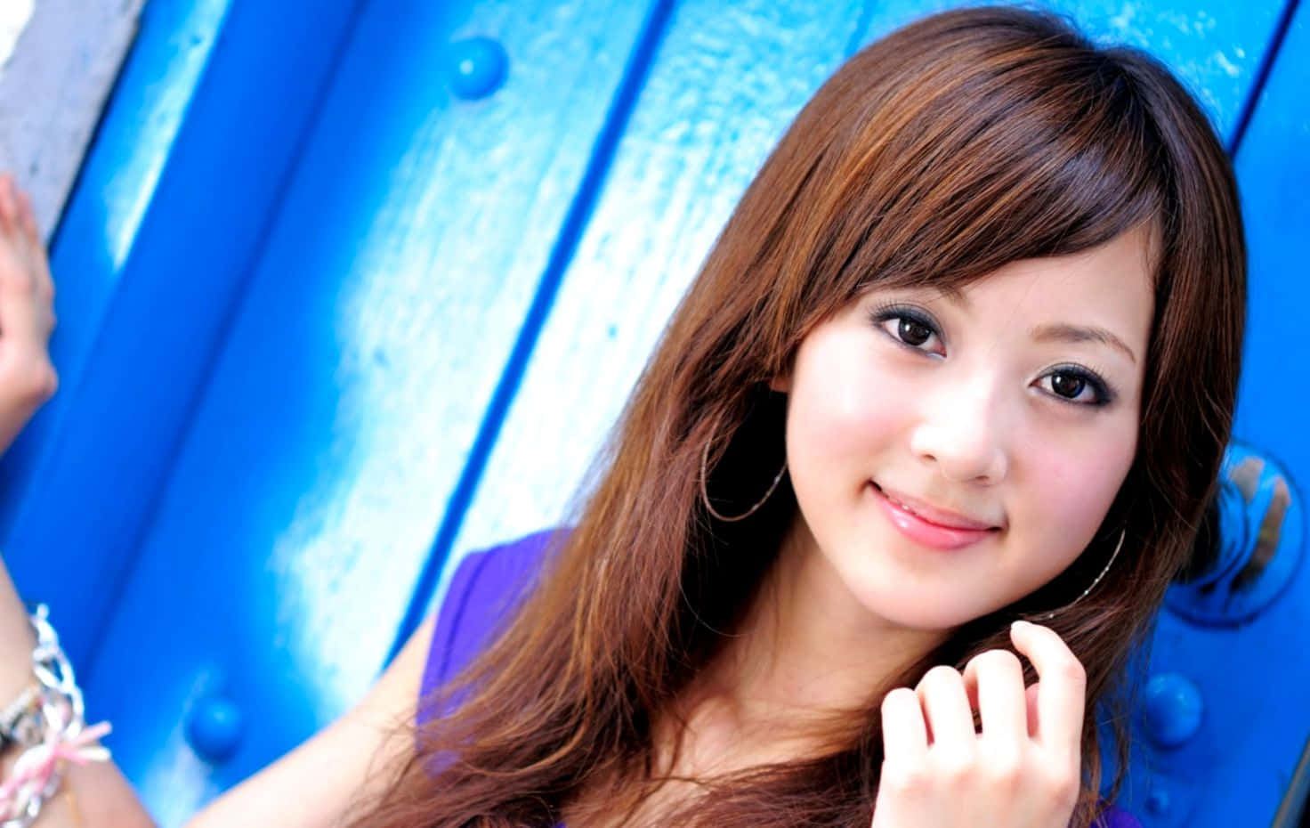 穿紫色上衣的可愛韓國女孩 壁紙 — 一位長著棕色長髮的年輕女子在充滿活力的藍色波紋金屬牆前溫柔微笑。
