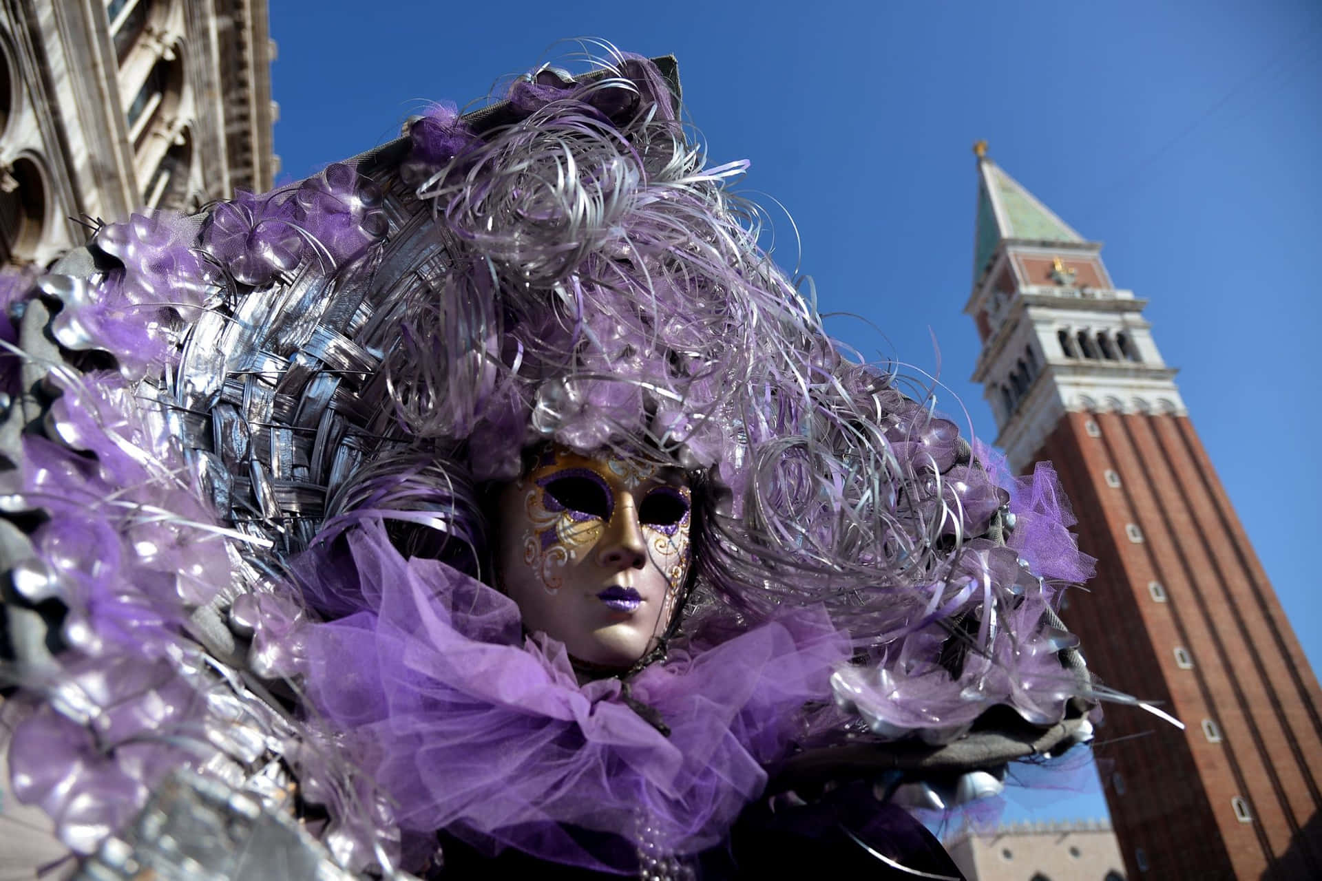 日落時分，聖馬可鐘樓附近穿著紫色和銀色服飾的威尼斯面具狂歡者。