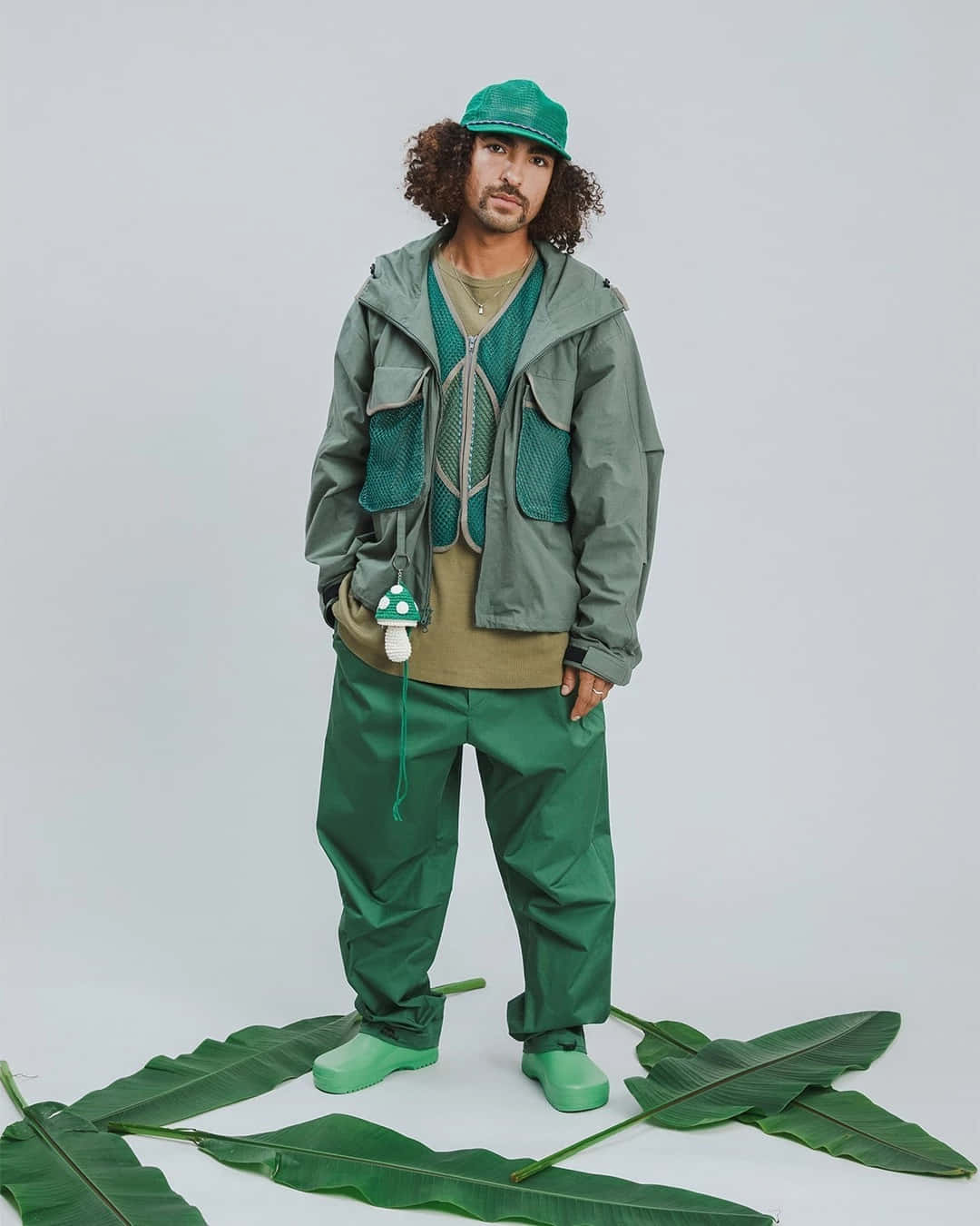 穿綠色褲子戴帽子的男人站在葉子旁 壁紙