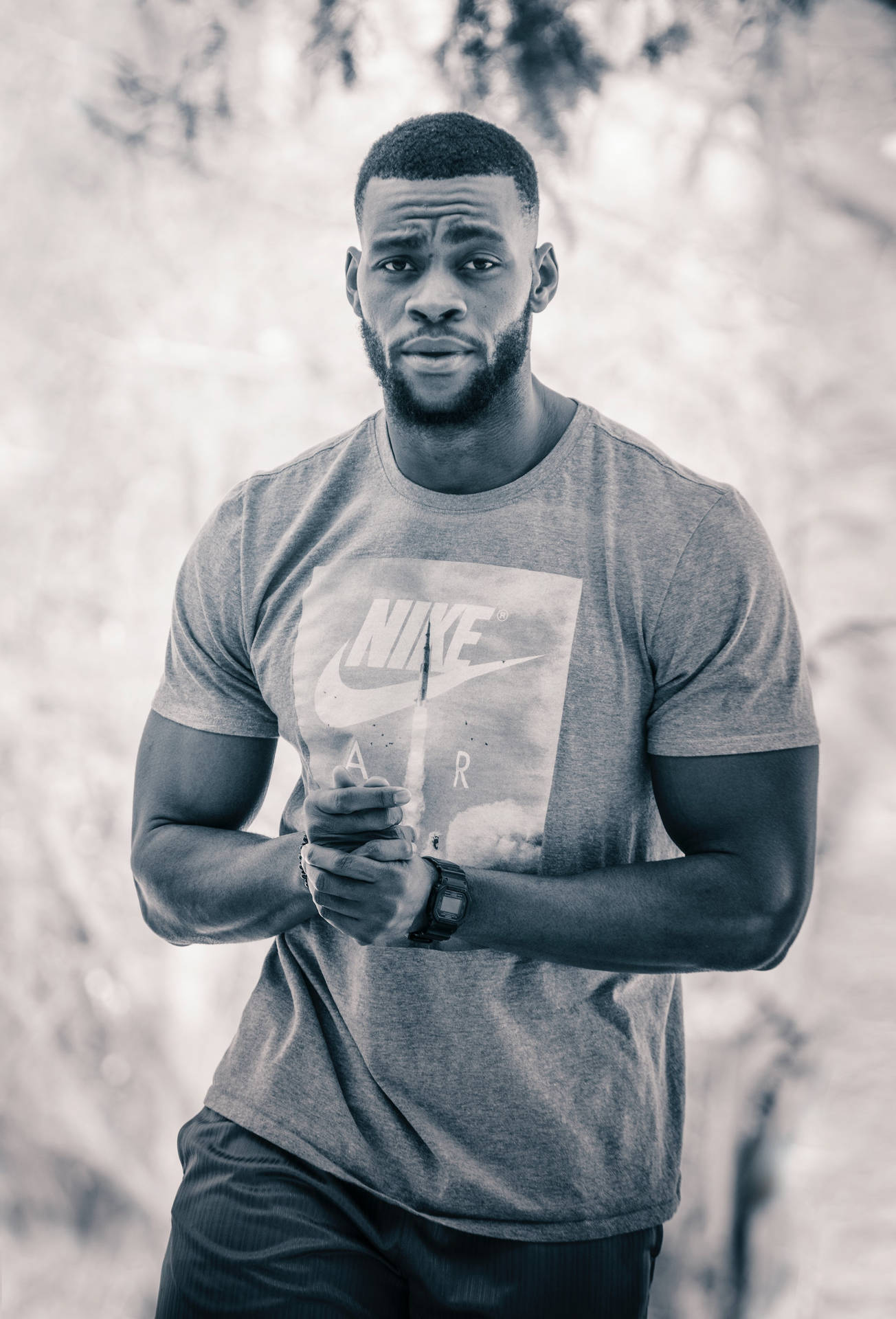 一個健壯的黑人男子穿著Nike T恤，雙手交疊站在戶外。