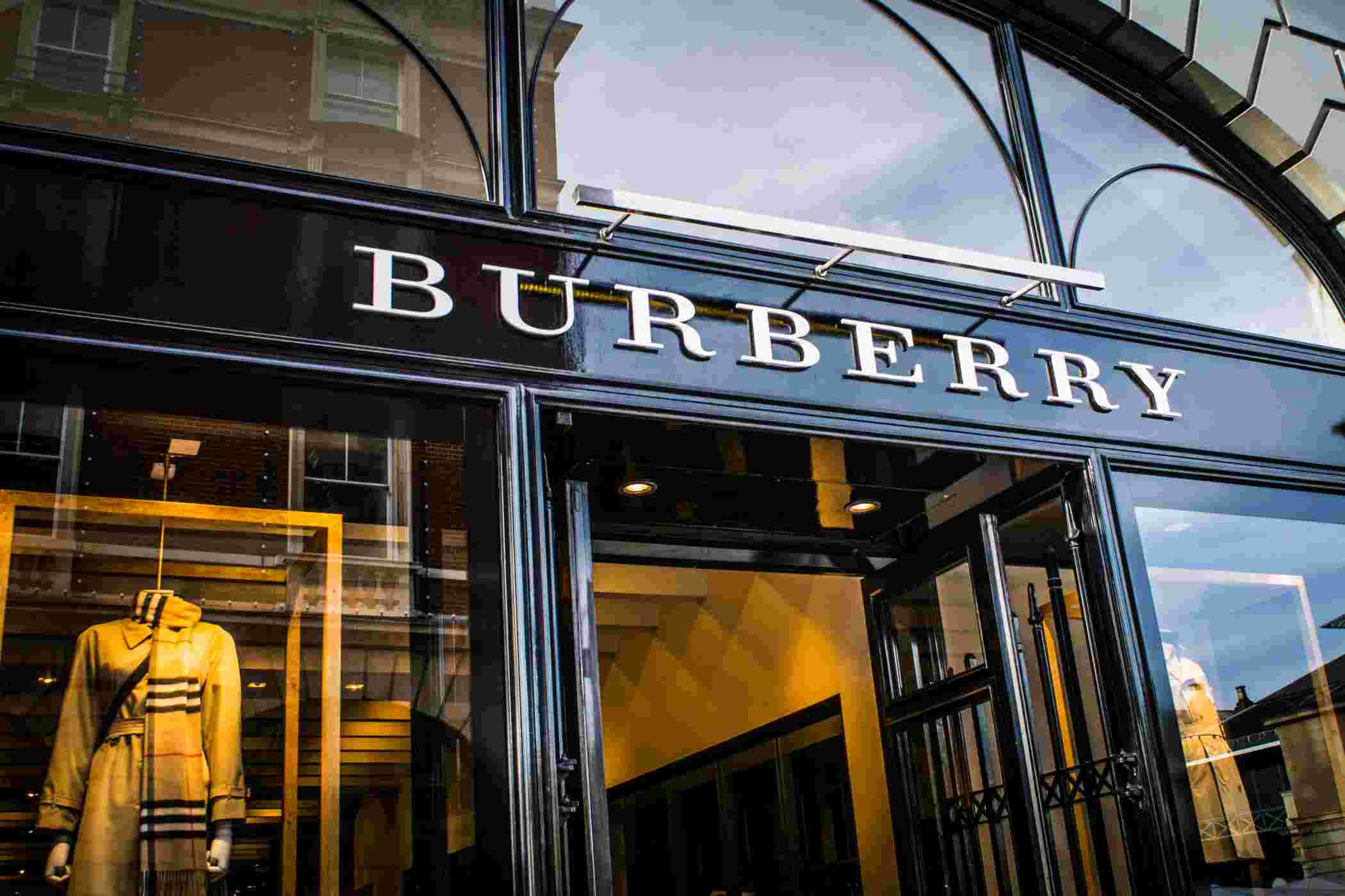 穿著 Burberry，展現清新現代感 壁紙 — 時尚的 Burberry 店舖外牆，配有玻璃門和經典風衣模特兒，在溫暖的室內燈光下展示。