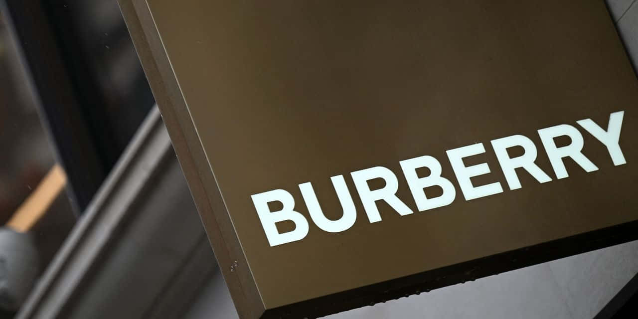 穿著 Burberry 格紋印花的時尚女性 壁紙 — 現代建築外牆上安裝的時尚棕色 Burberry 標誌特寫，帶有粗體白色字體。