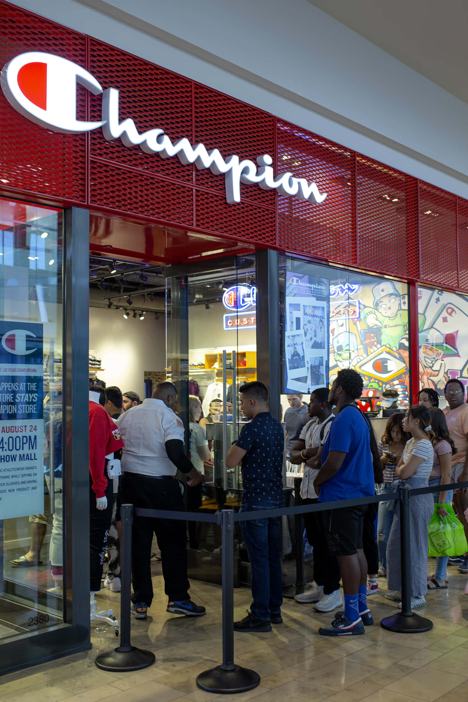 穿著 Champion，感覺很棒 壁紙 — 人群在商場內一間亮紅色Champion商店外排隊，商店有玻璃門，牆上佈滿色彩繽紛的塗鴉藝術。
