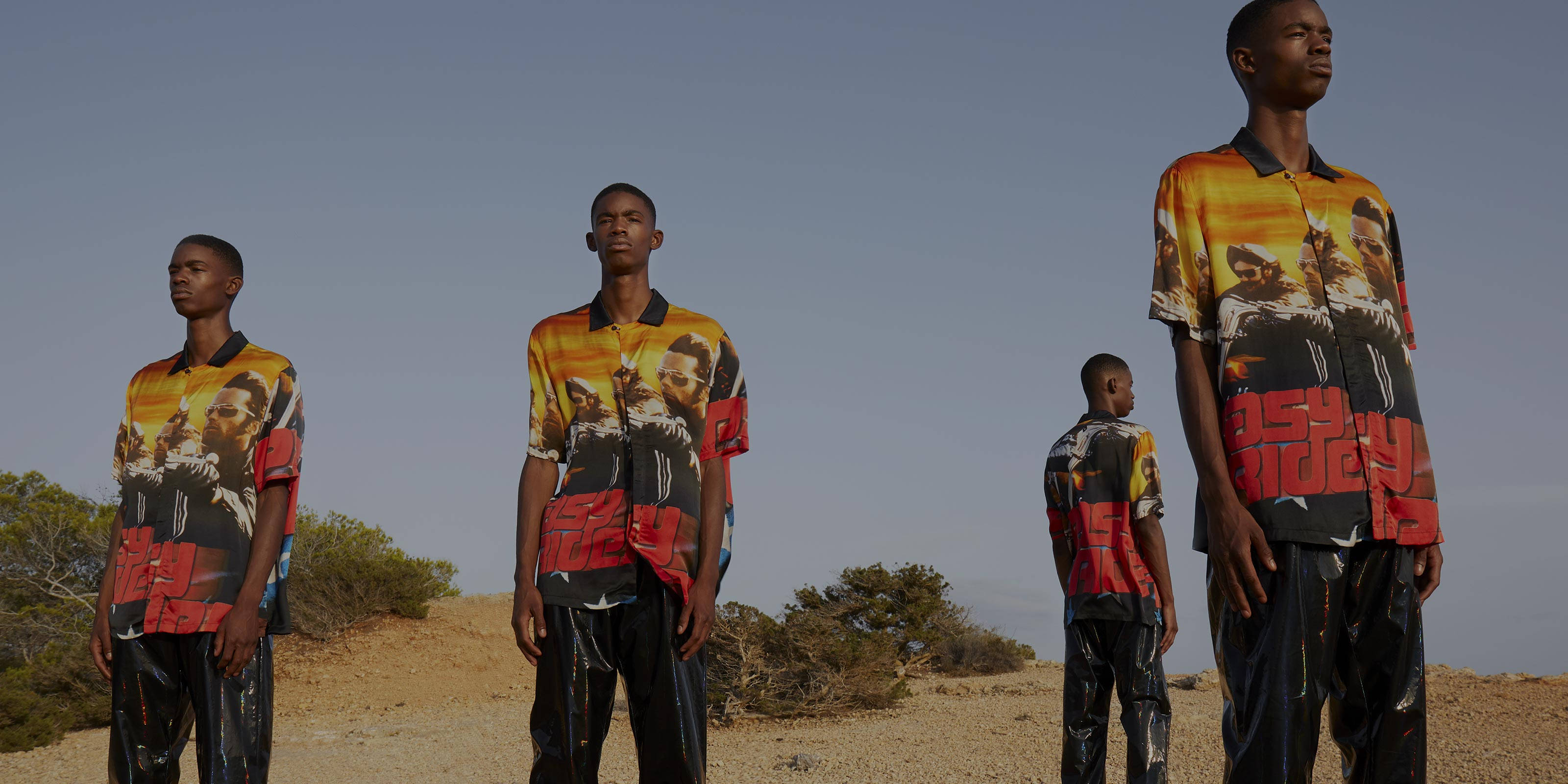 穿著 Marcelo Burlon 的黑人模特 壁紙 — 四個穿著大膽圖案襯衫的男人站在晴朗天空下的乾燥沙漠景觀中。