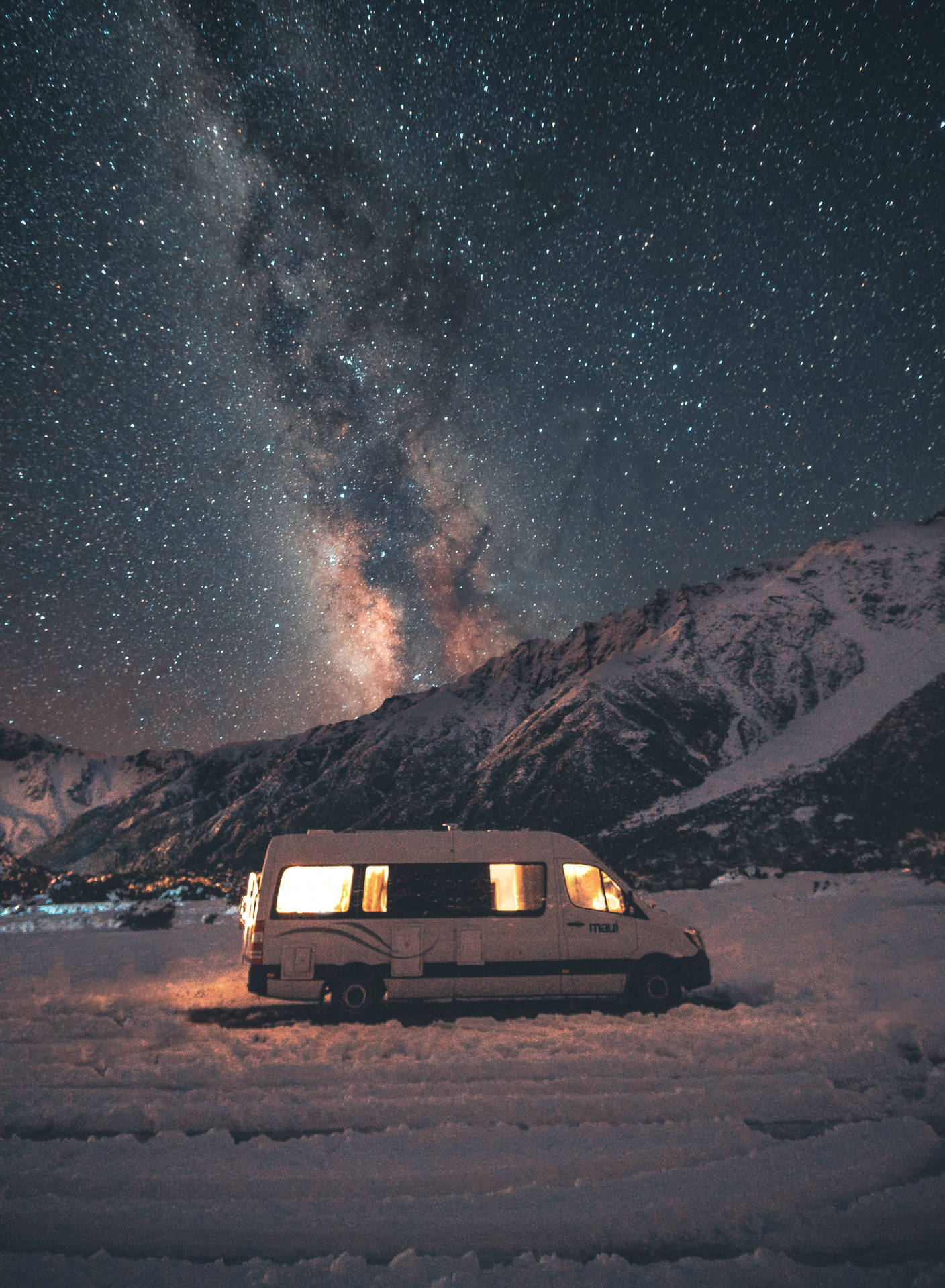 一輛露營車停在雪地中，窗戶在星空和銀河下發光。